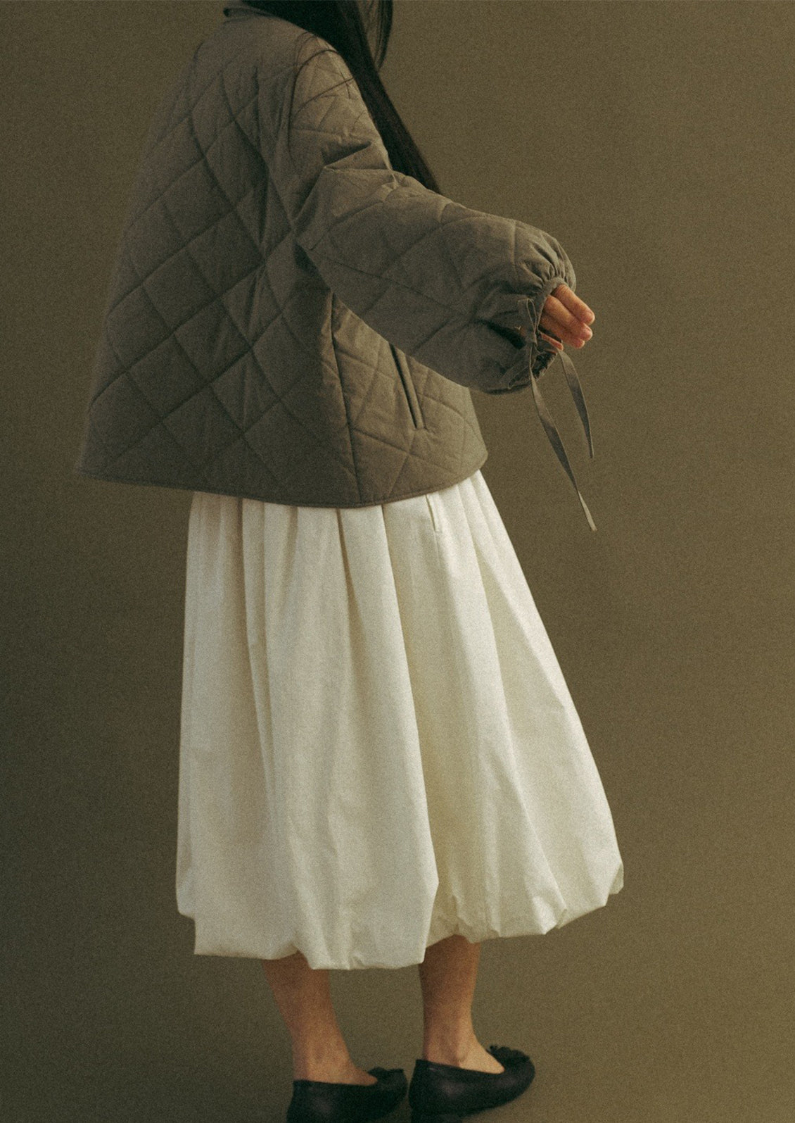 A woman wearing a quilted, padded jacket in army green with tie detail at wrists.