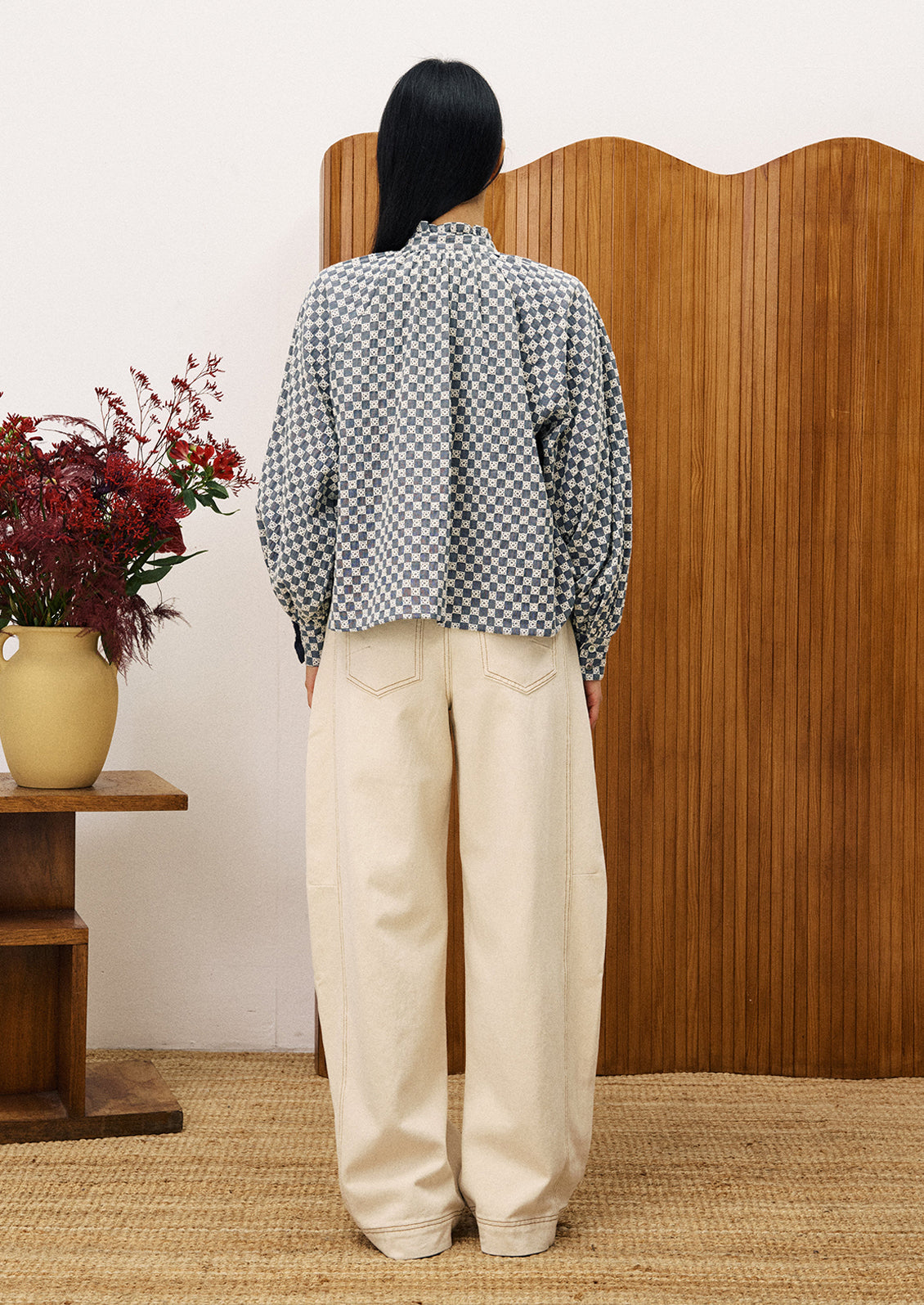 A woman wearing a ruffle neck blouse with embroidered white check pattern.