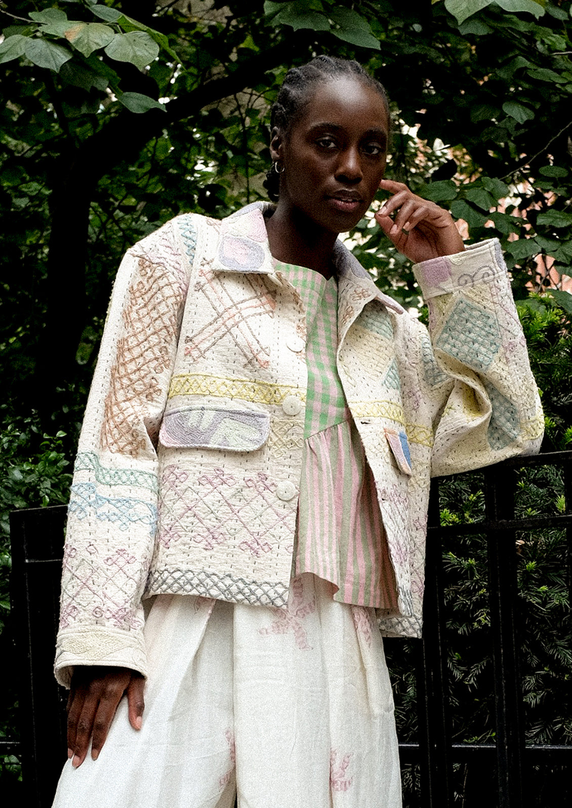 A person wearing a cream jacket with allover pastel embroidery.