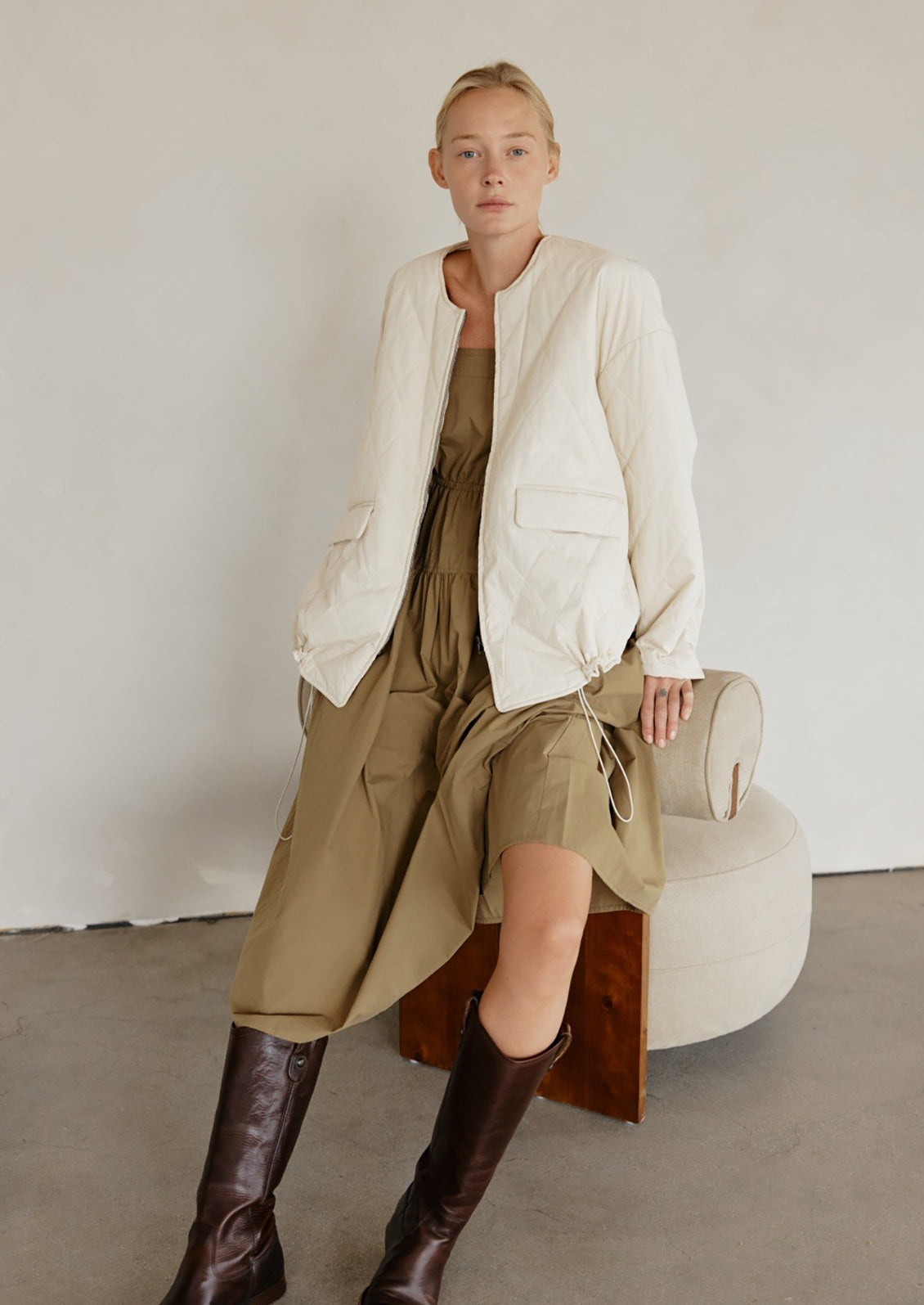 A woman wearing a padded quilted jacket with bottom drawstring detail in cream.