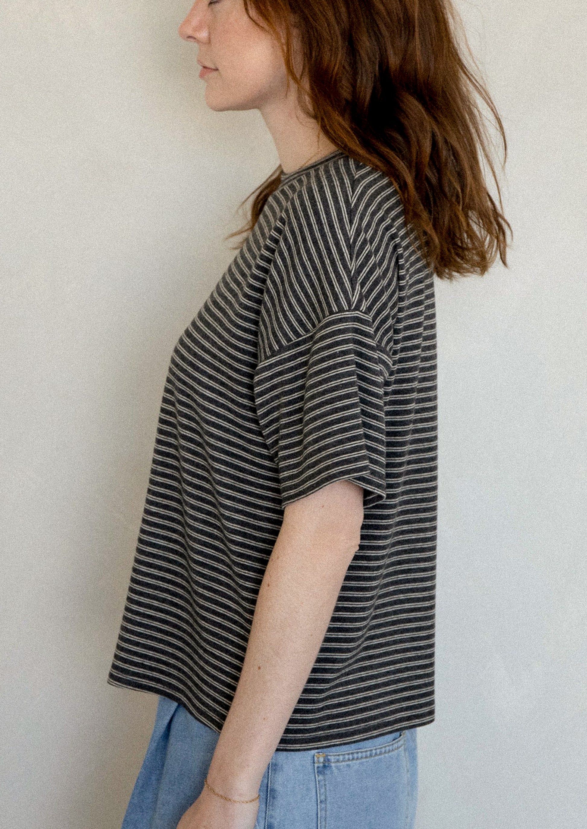 A woman wearing a slouchy t-shirt in charcoal with thin white stripes.