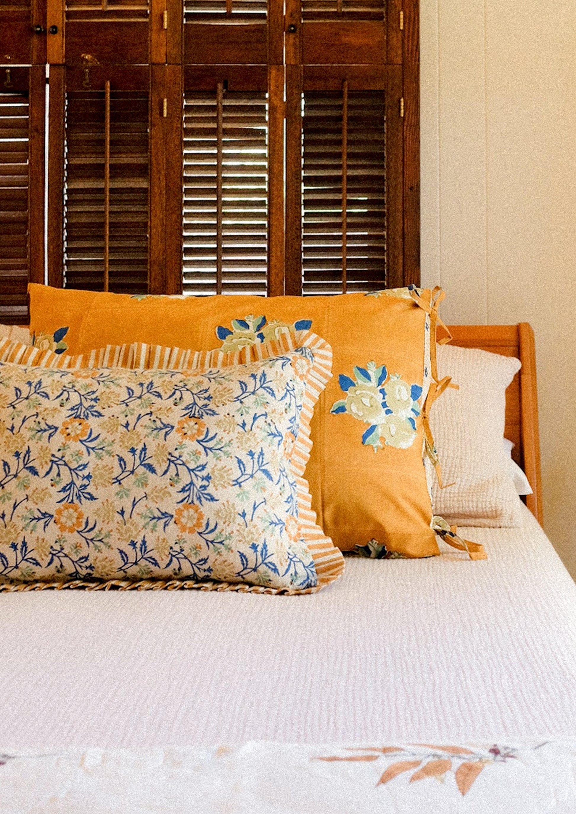 Decorative pillows on a bed with wooden shutters in the background