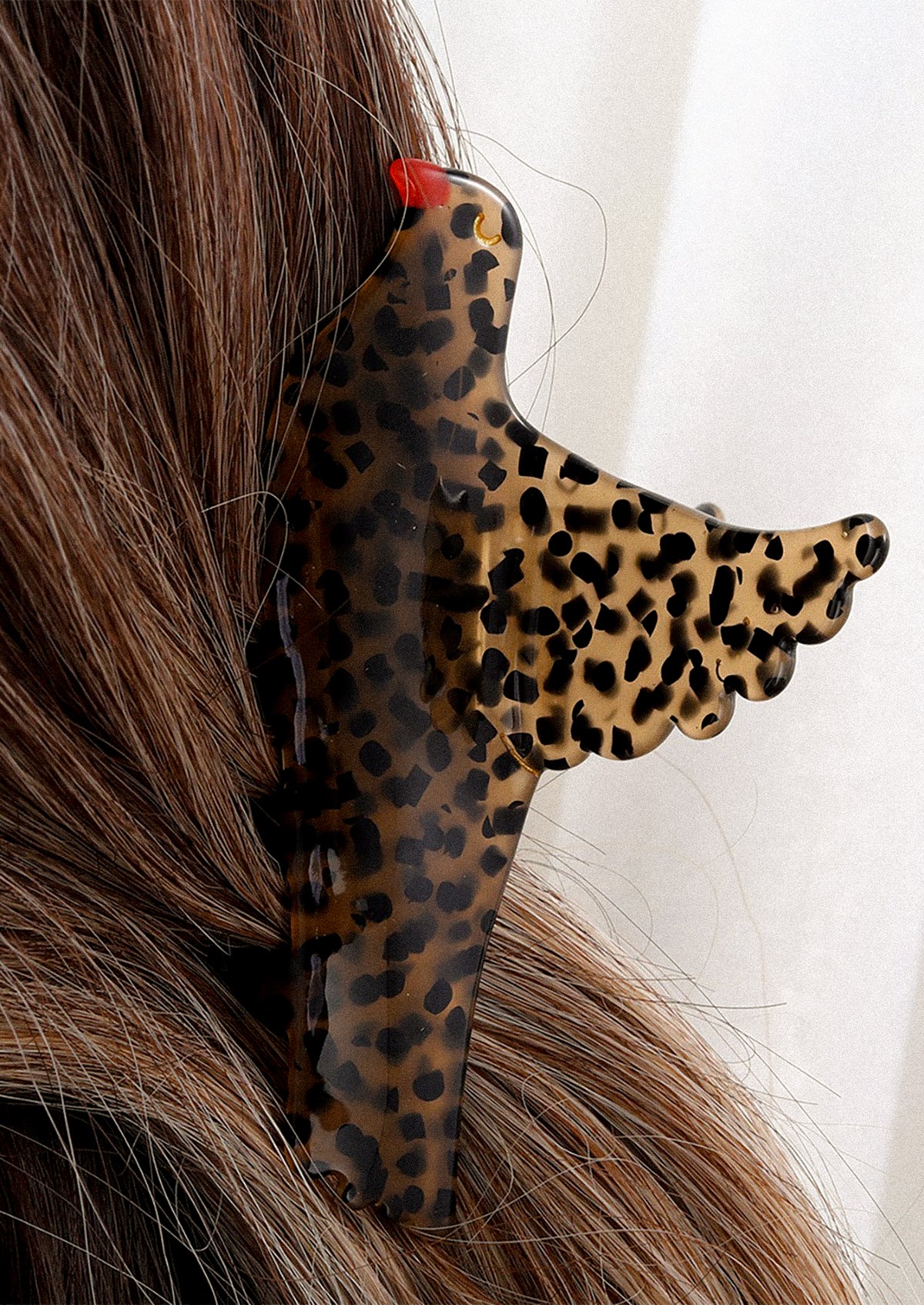 A person wearing a hair claw of brown bird with black spots and red beak.
