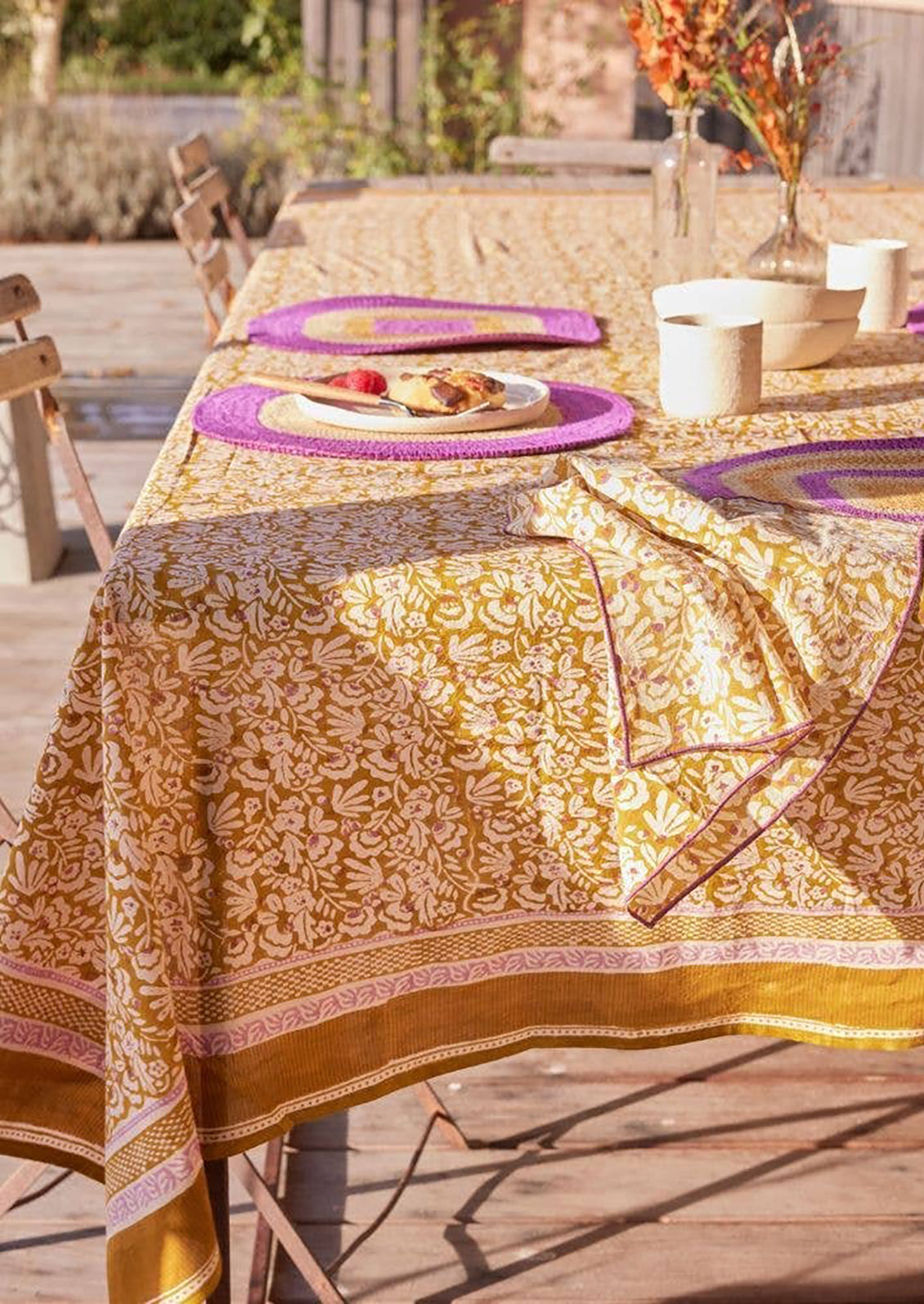 A block printed tablecloth with striped border and floral center in ochre and magenta color palette.
