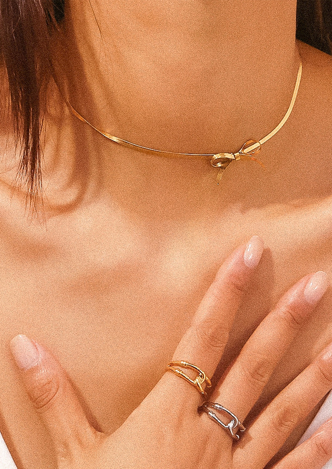 A woman wearing a gold choker-style necklace with bow shape at front.