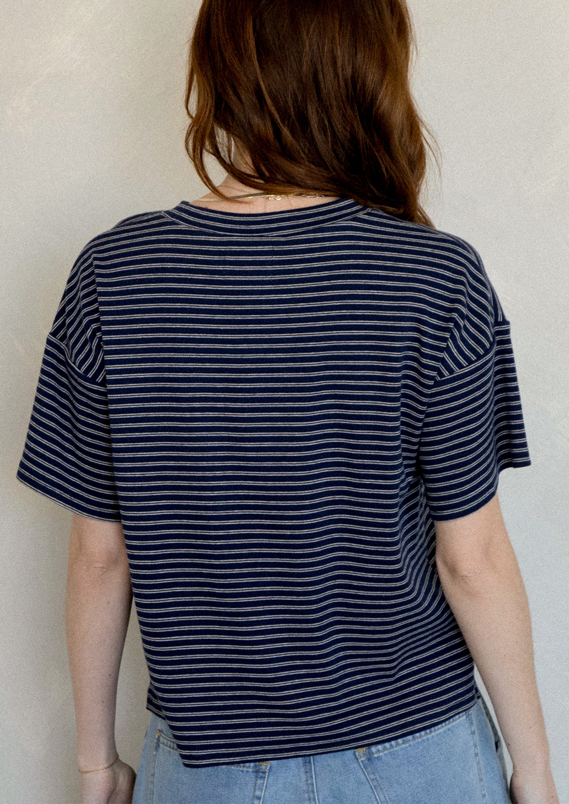 A woman wearing a slouchy t-shirt in navy with thin white stripes.