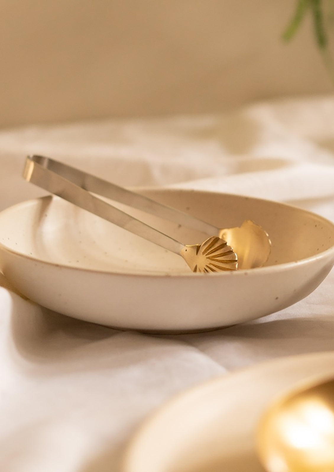 A pair of stainless steel serving tongs with brass seashell tip.