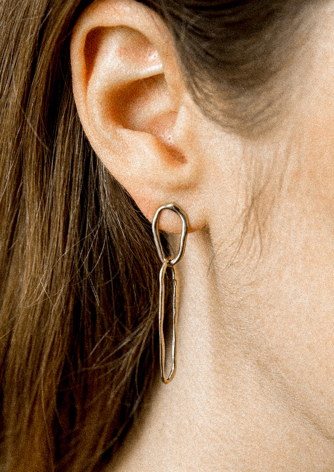 A person wearing a pair of sterling silver earrings with two amorphous link shapes connected.