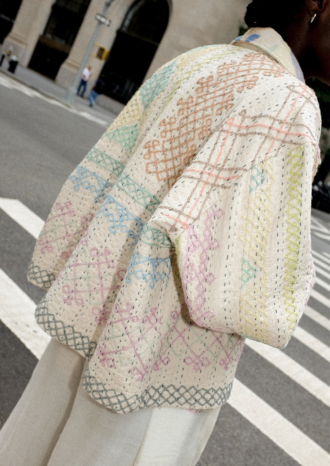 A person wearing a cream jacket with allover pastel embroidery.