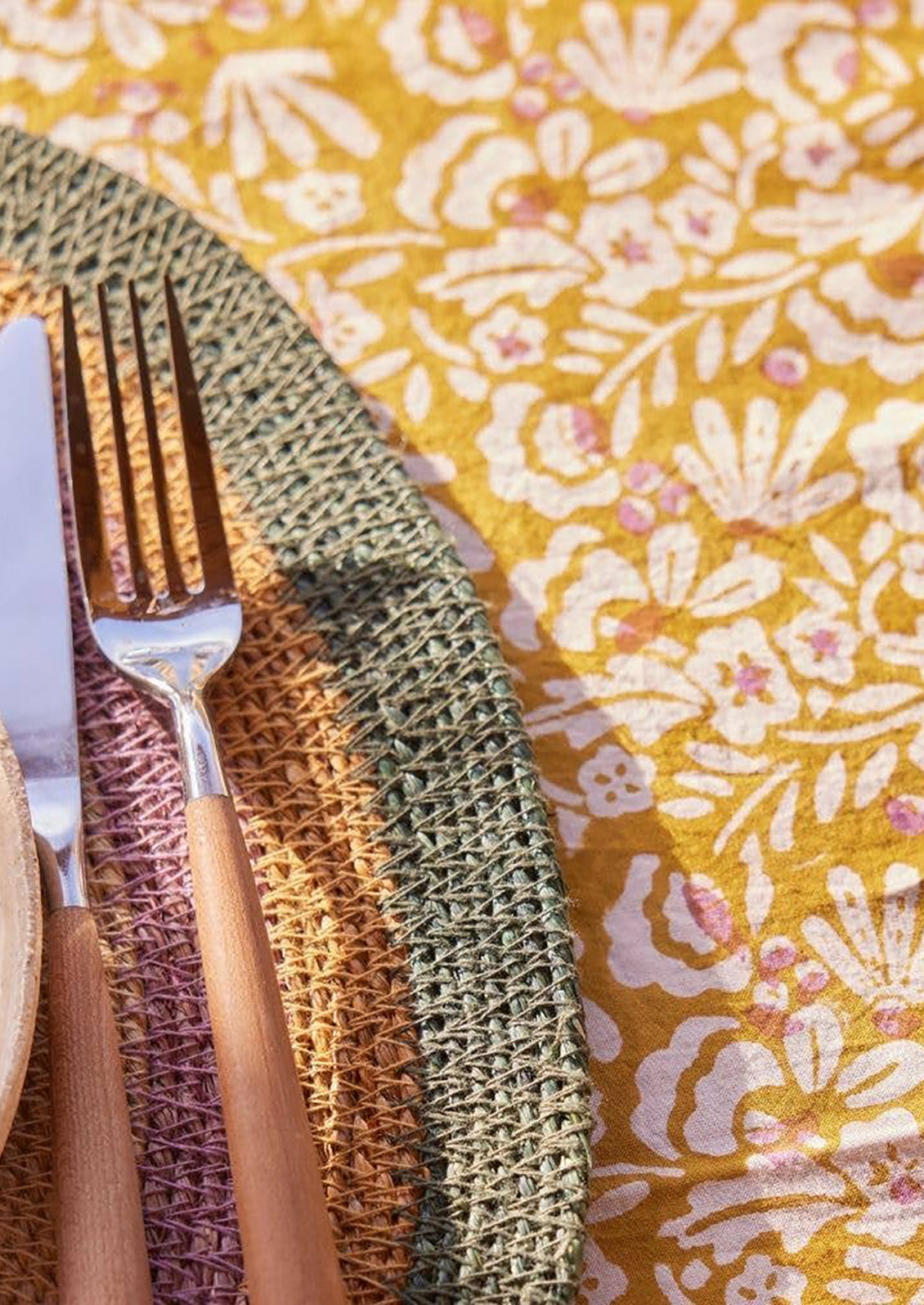 A block printed tablecloth with striped border and floral center in ochre and magenta color palette.