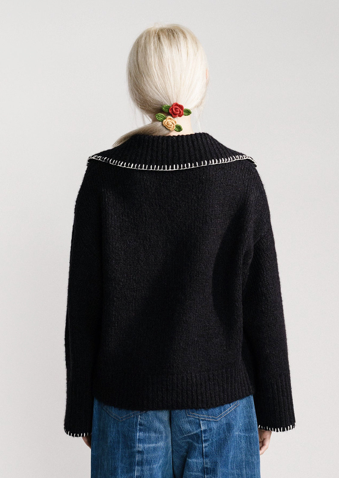 A woman wearing a black sweater with notched collared v-neckline and wide bell sleeves.