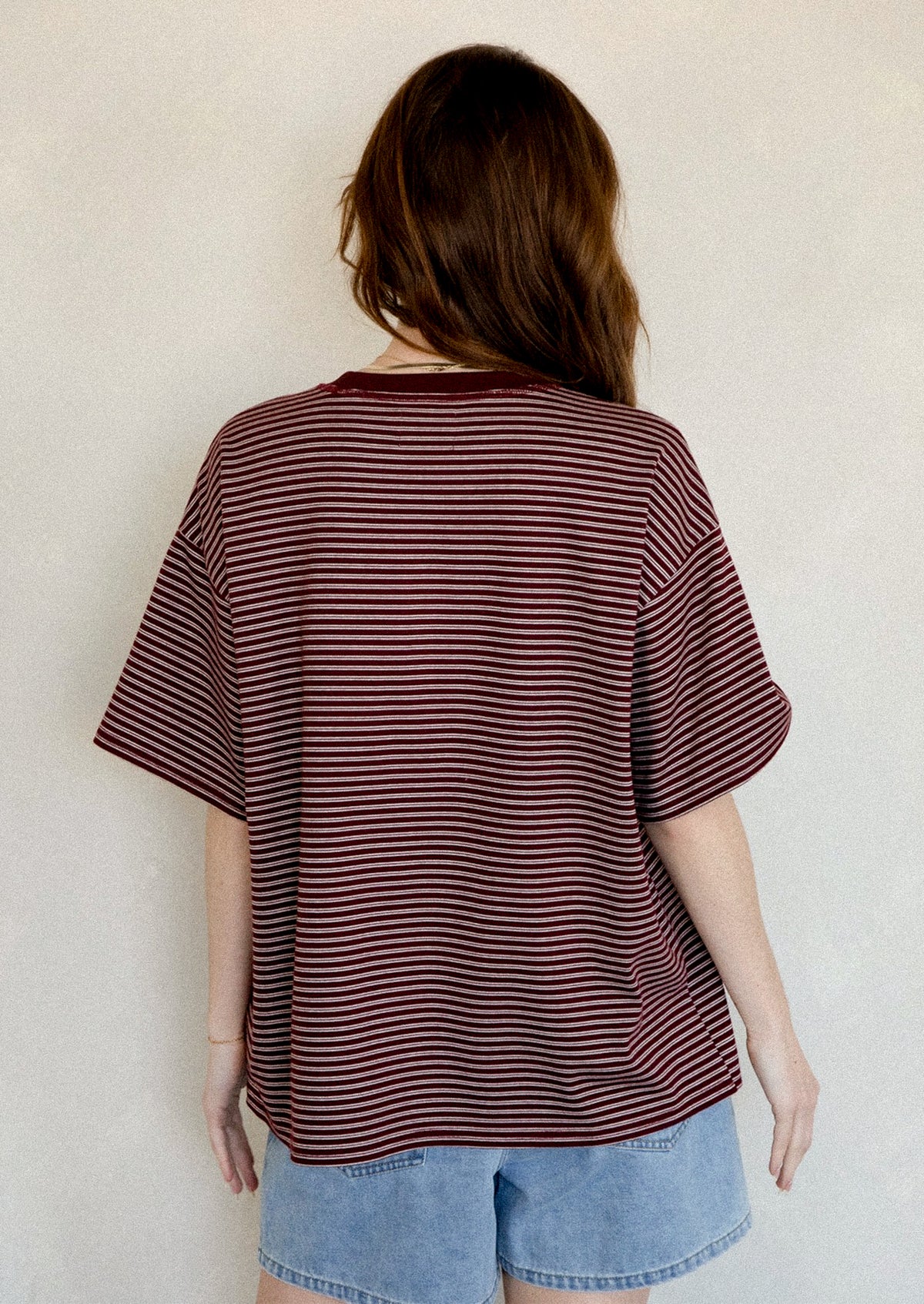 A person wearing an oversized t-shirt in maroon with white stripes.