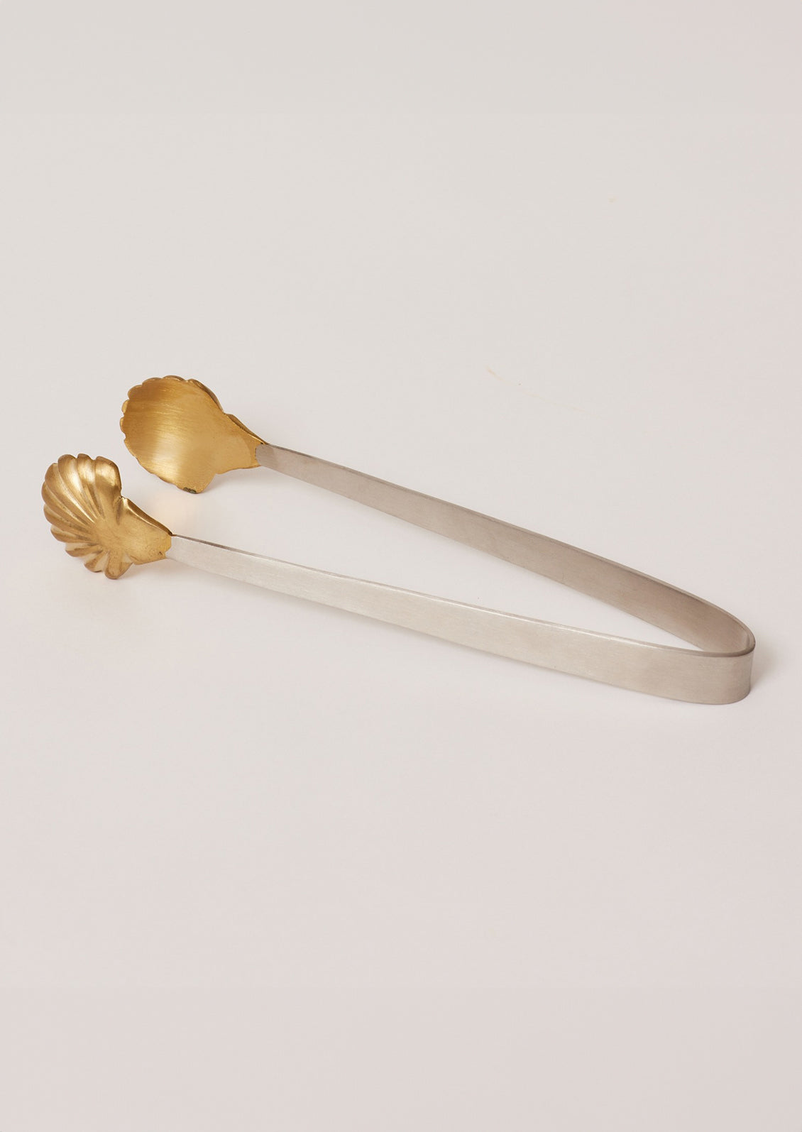 A pair of stainless steel serving tongs with brass seashell tip.
