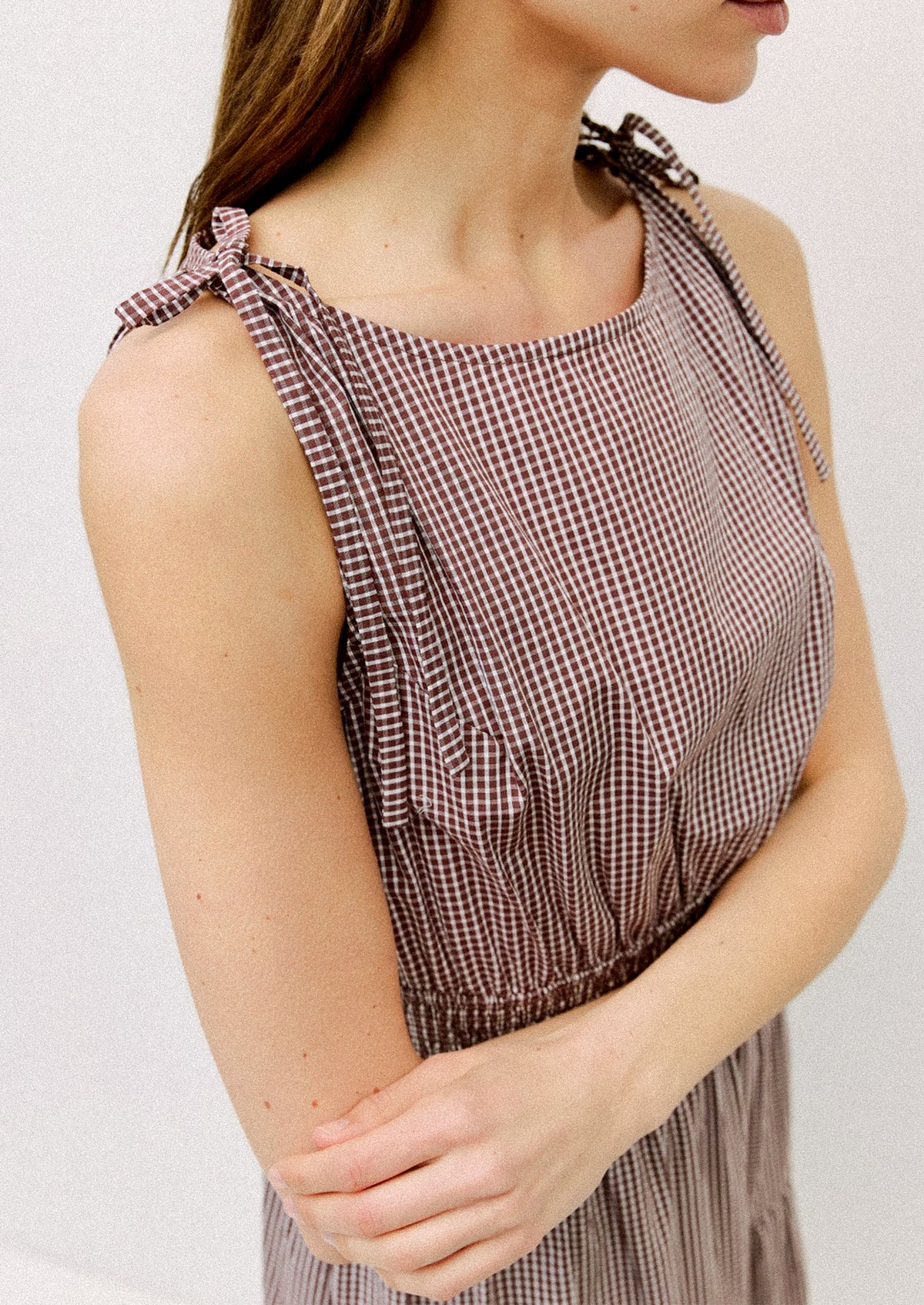 Woman wearing a sleeveless checkered dress with bow straps on a plain background