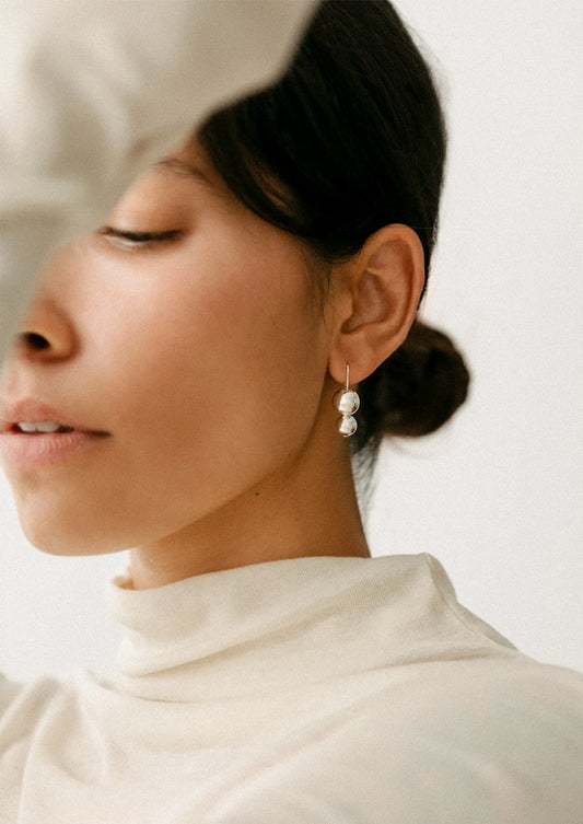 A woman wearing a pair of silver earrings in the shape of stacked orb.