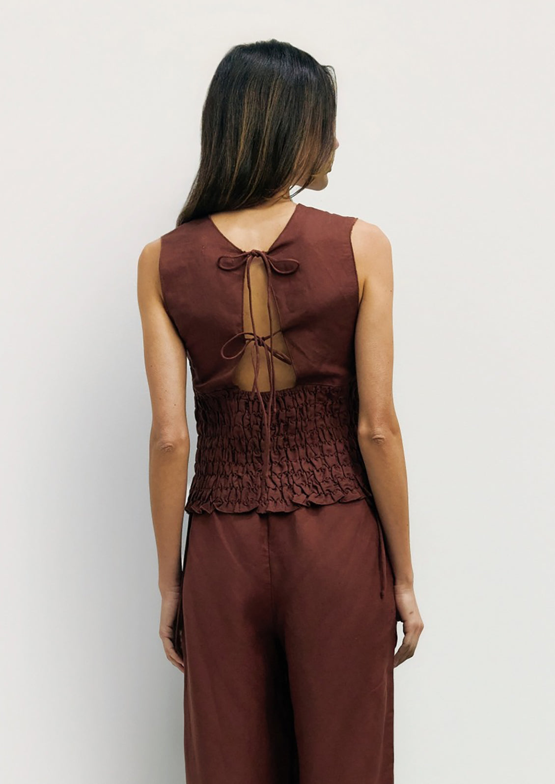 Woman wearing a brown sleeveless top and pants against a white background