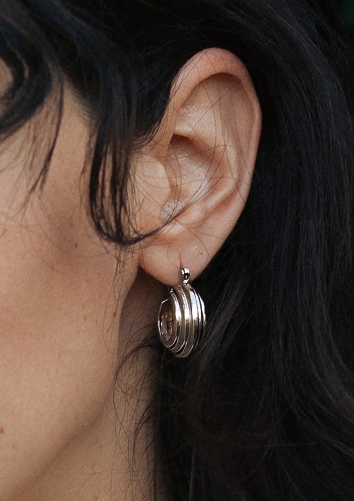 A person wearing a pair of ribbed circular hoop earrings.