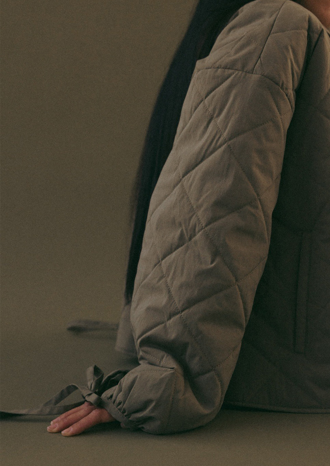 A woman wearing a quilted, padded jacket in army green with tie detail at wrists.