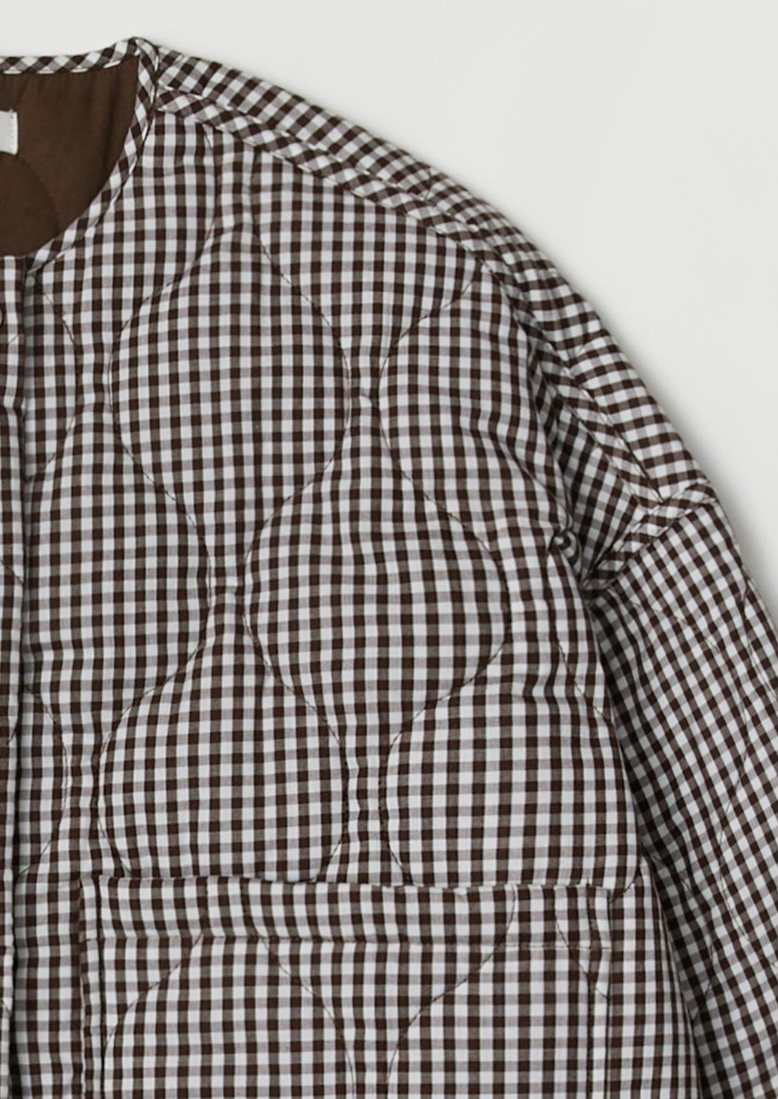 A woman wearing a quilted jacket in chocolate brown and white gingham.