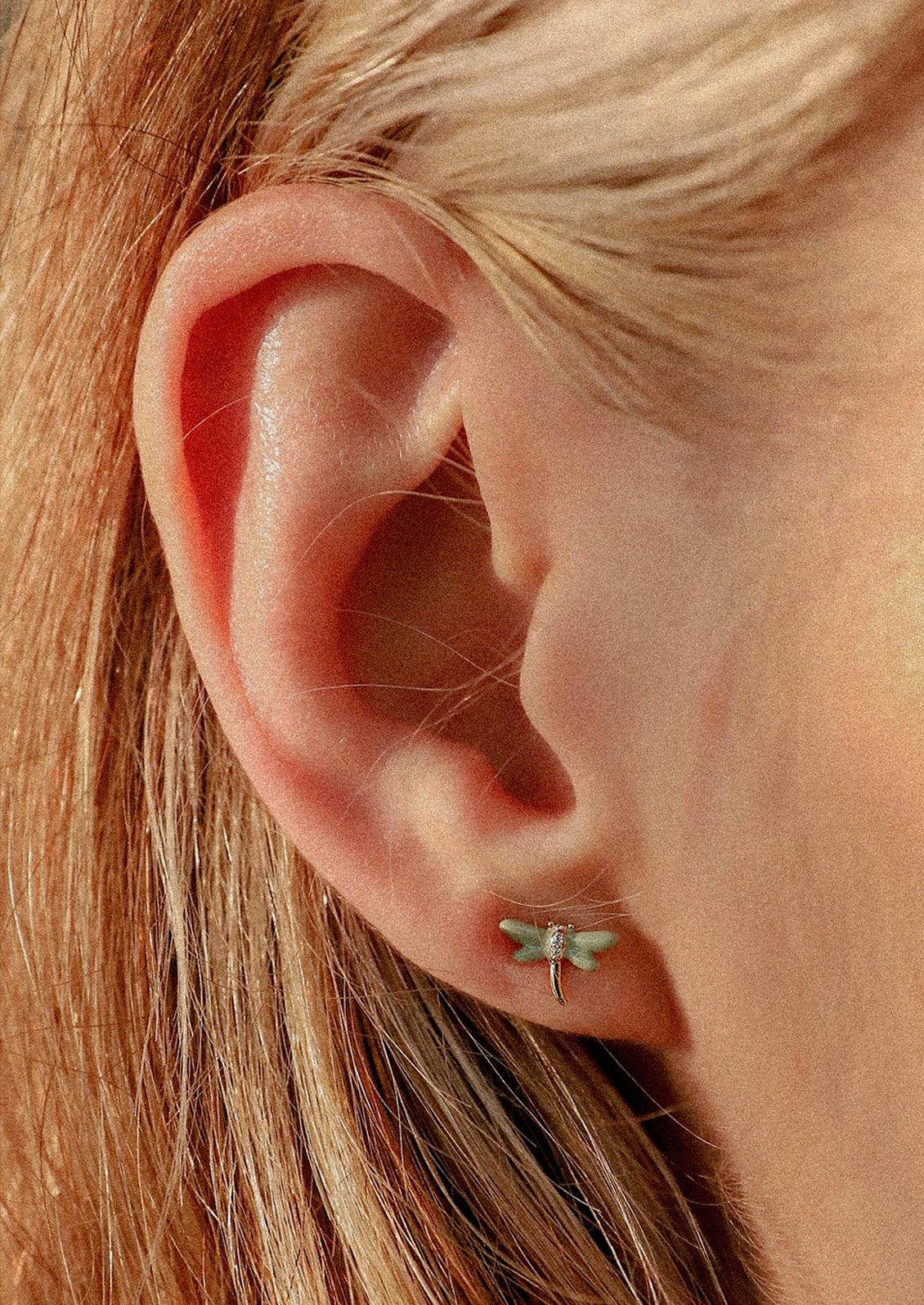 A woman wearing a small blue dragonfly stud earring.