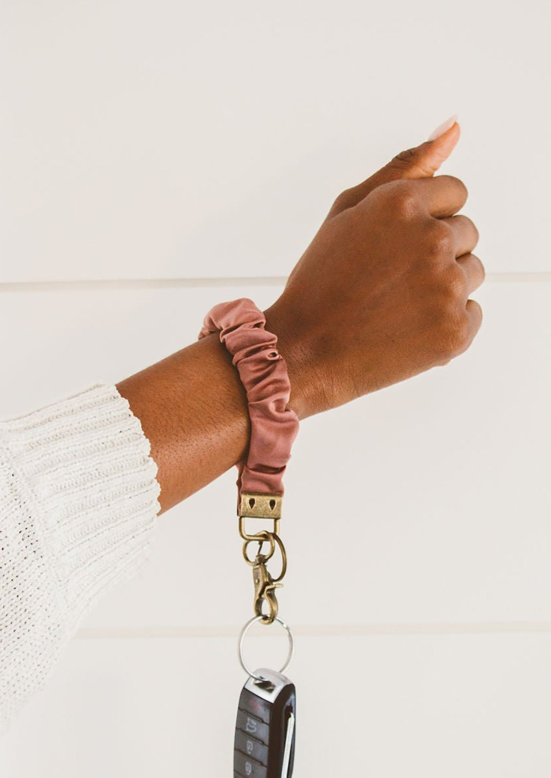 A dusty rose scrunchie wristlet keychain around a woman's wrist.