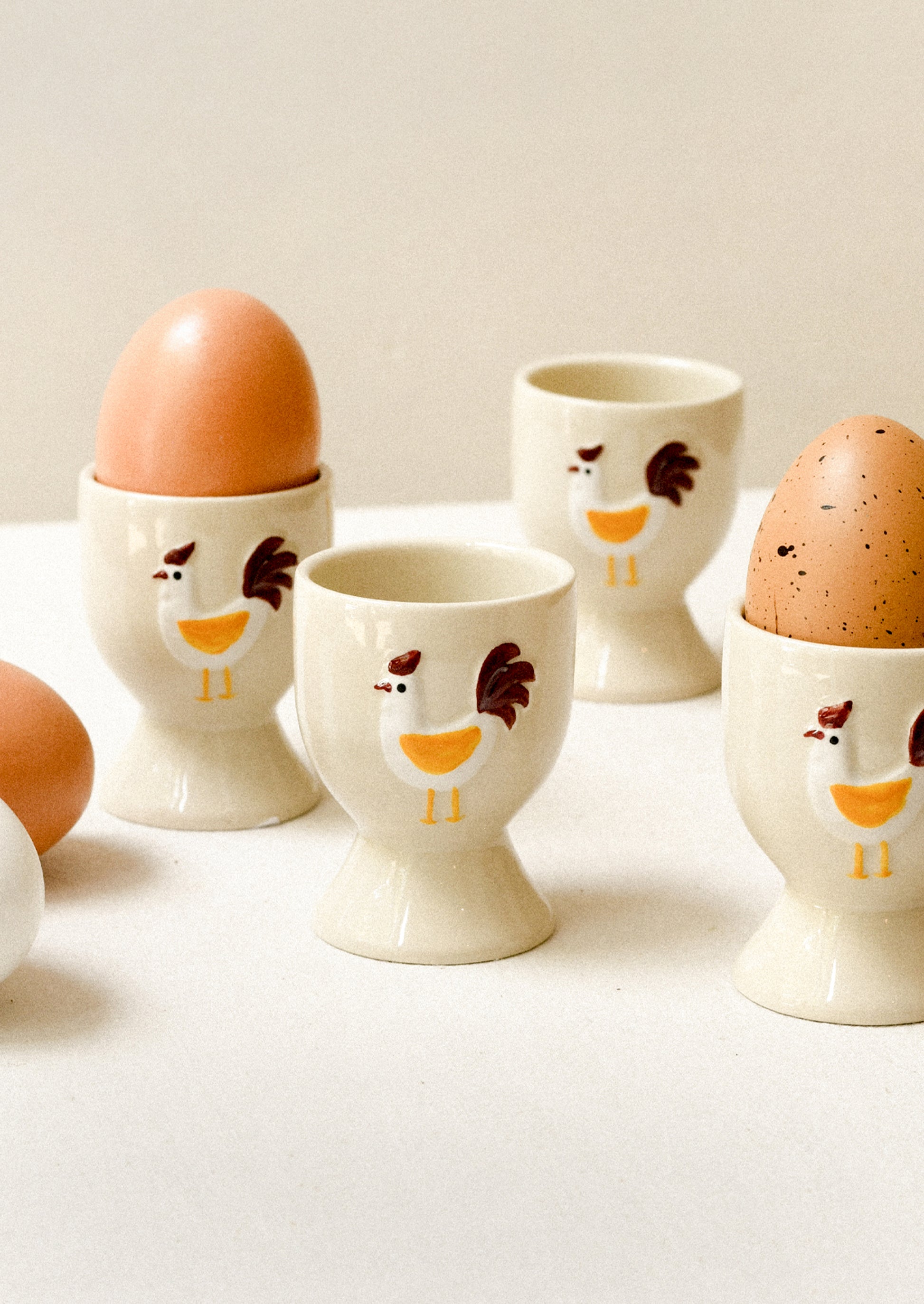 Set of four ceramic egg cups with chicken designs on a white surface.