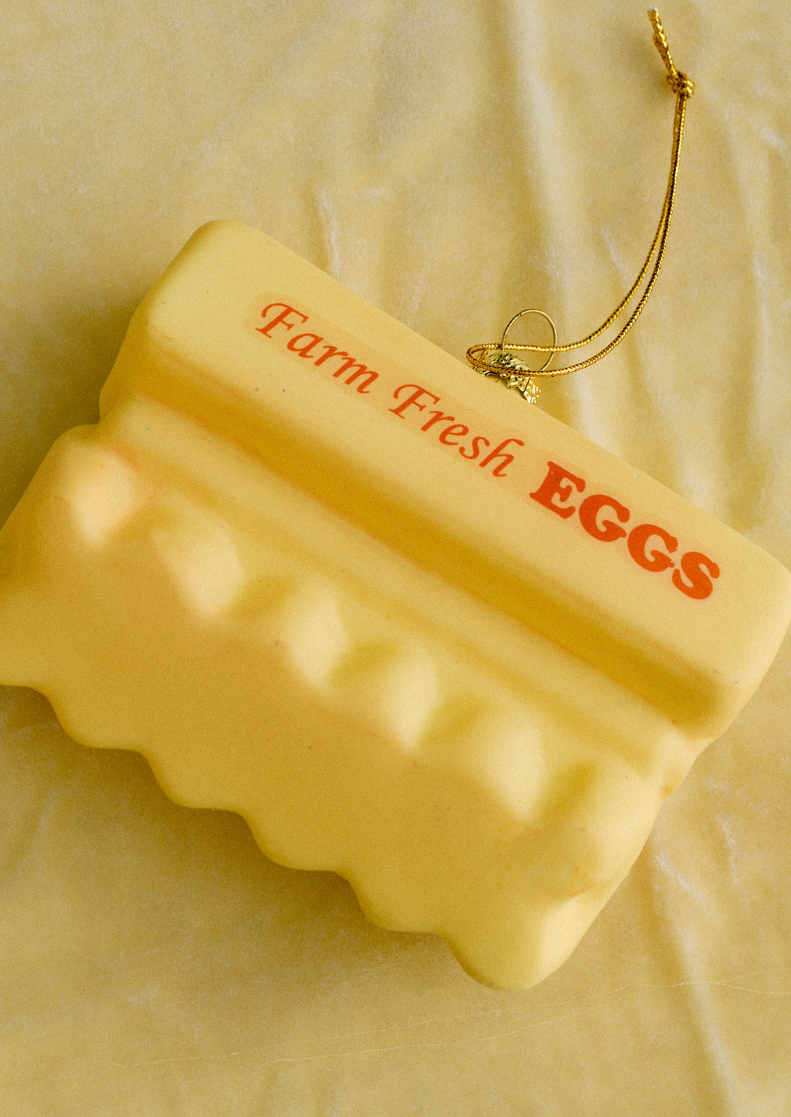 A glass ornament of yellow carton of a dozen multicolored eggs.