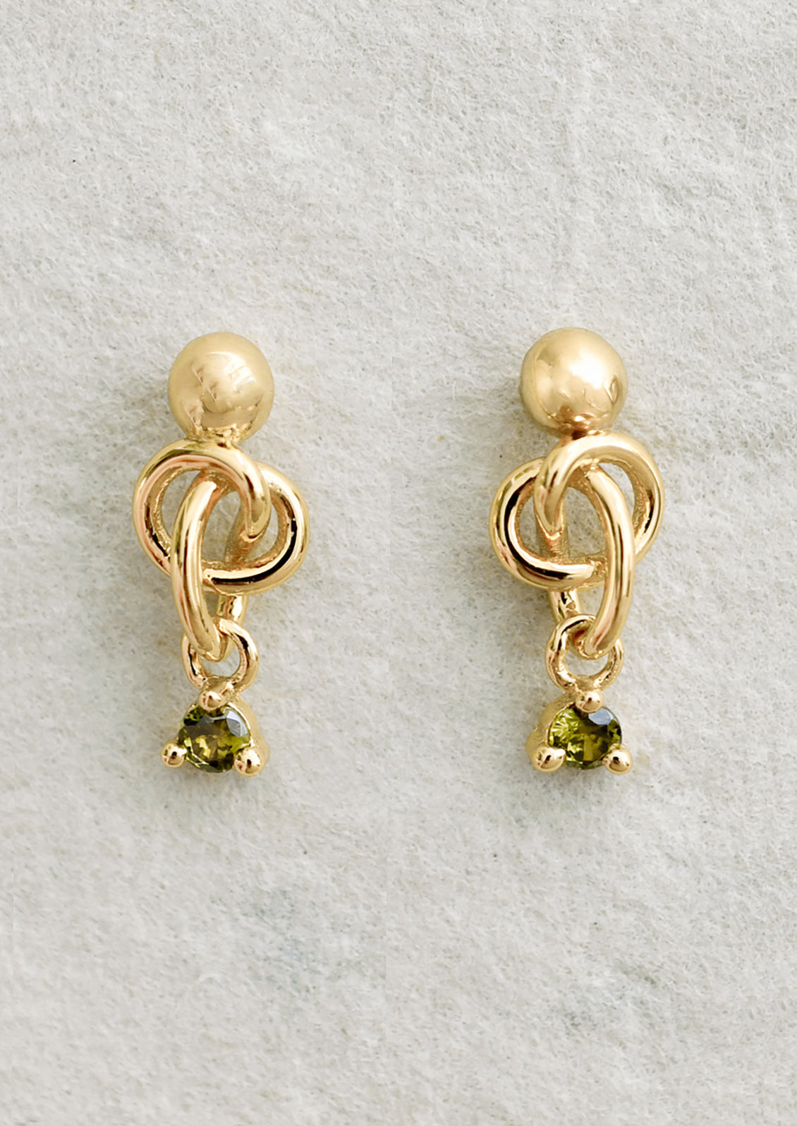A pair of ball stud earrings with knot and green crystal.