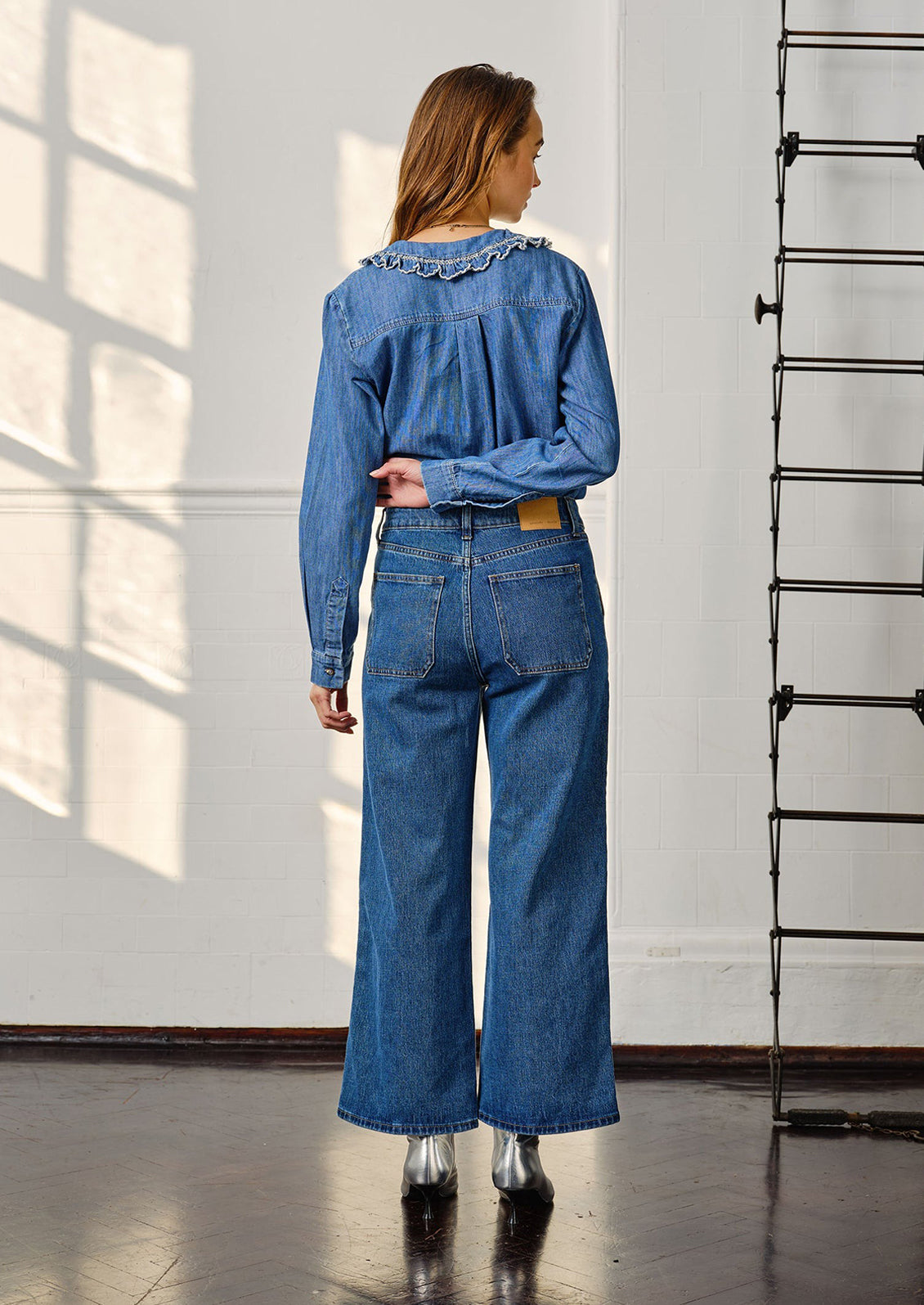 A woman wearing blue jeans with denim top and silver boots, seen from behind. 