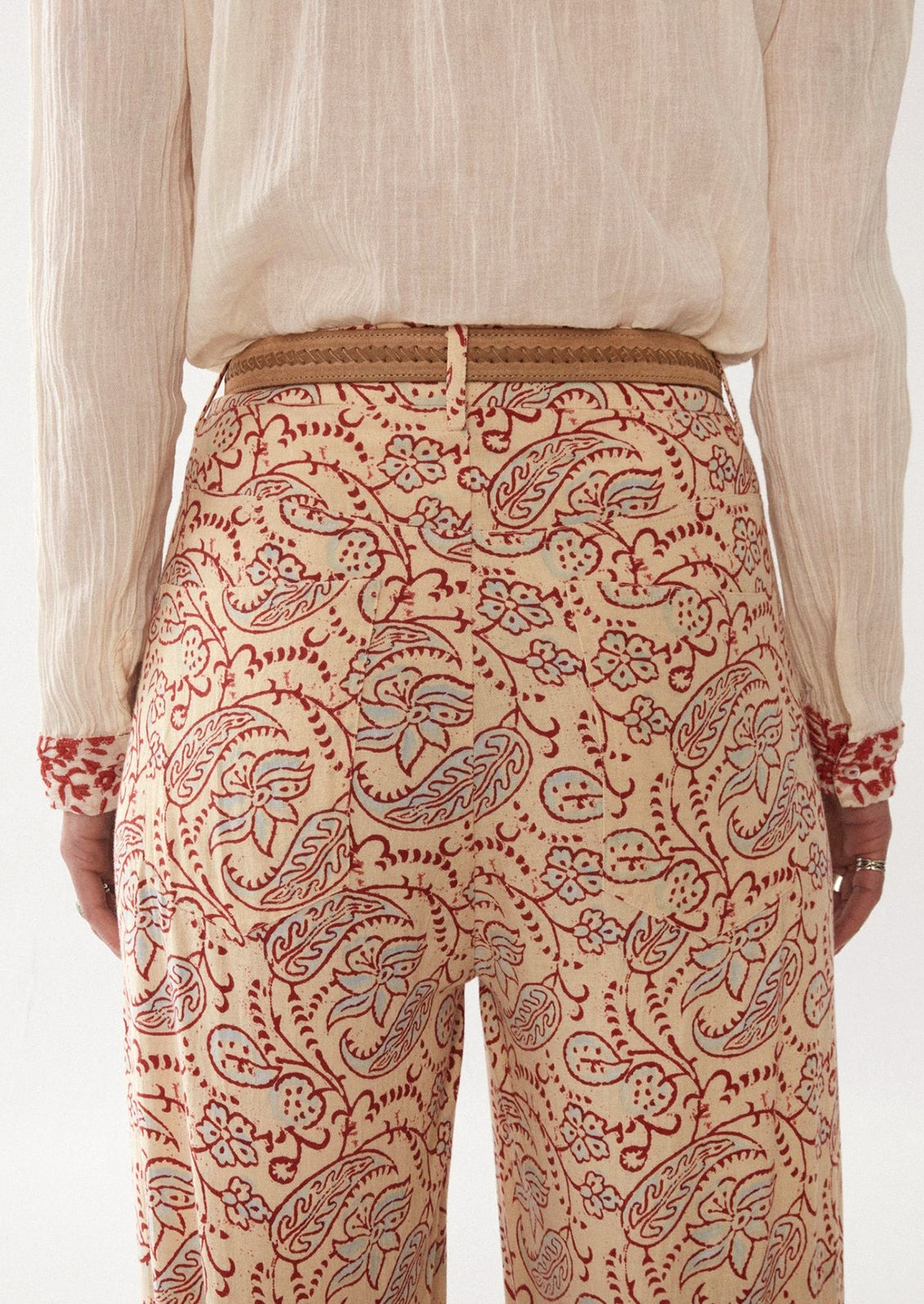 Woman wearing cream, red, and blue paisley printed pants, seen from behind. 