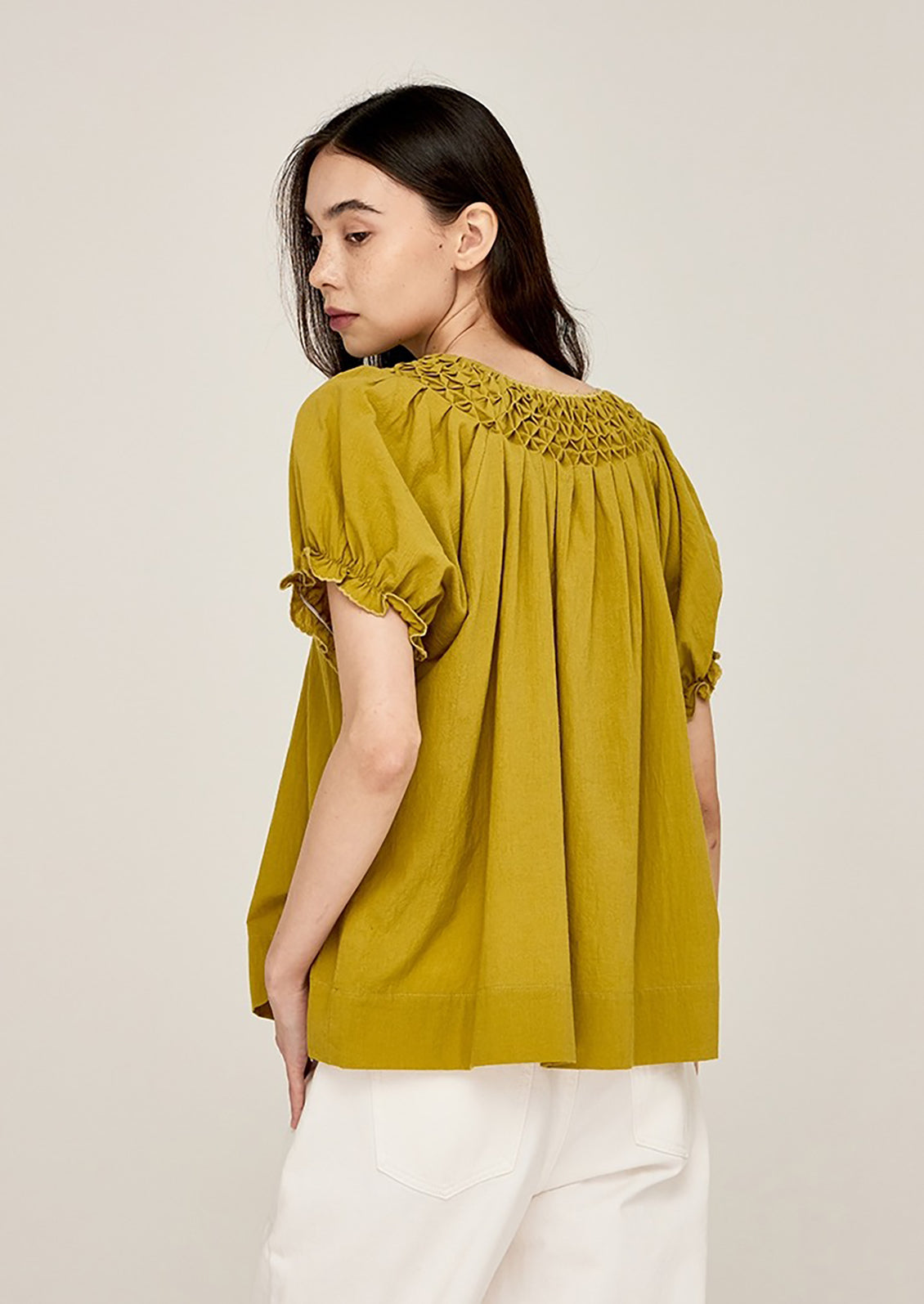 A woman wearing a lime green shirt with smocked detailing at neck.