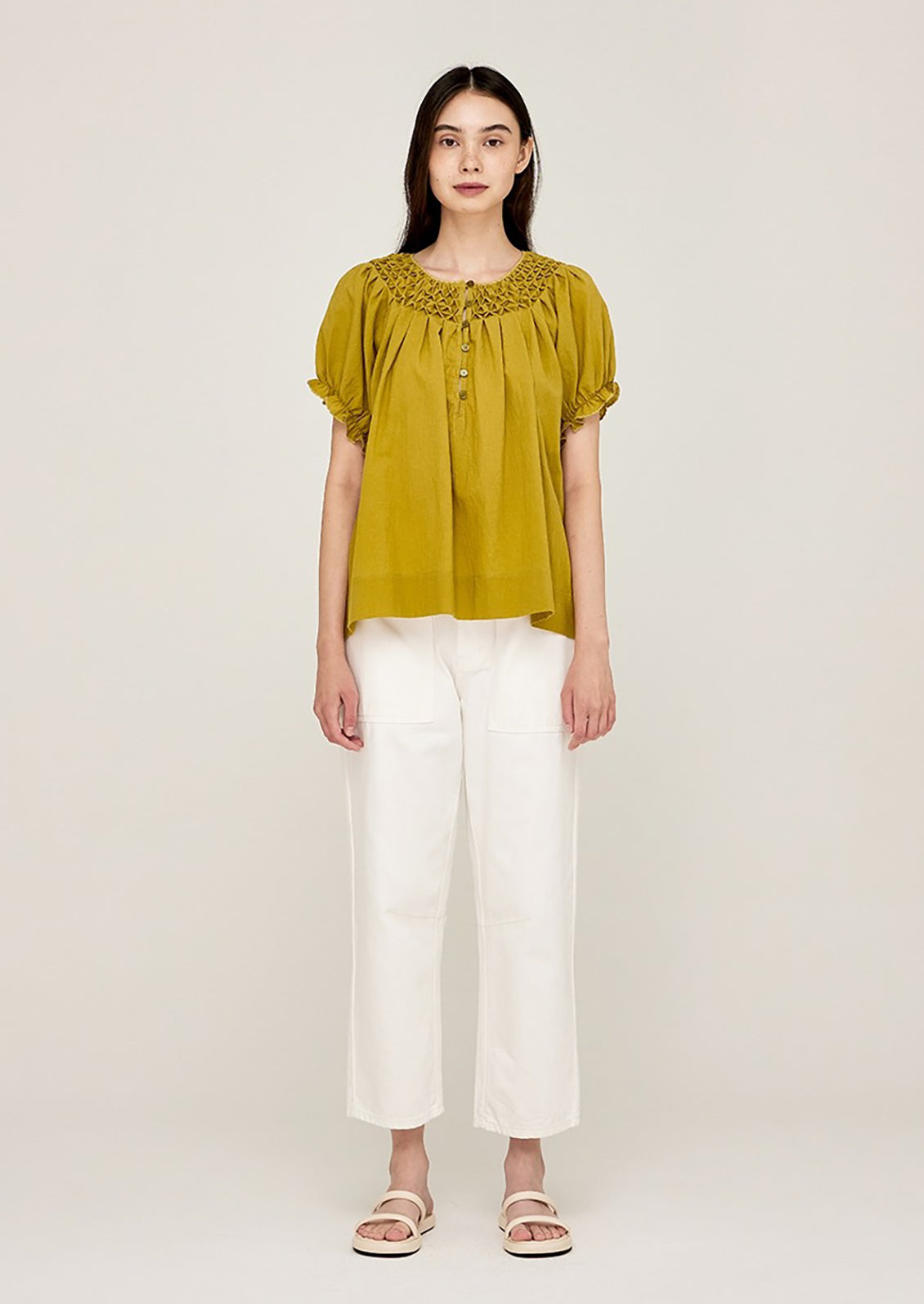 A woman wearing a lime green shirt with smocked detailing at neck.