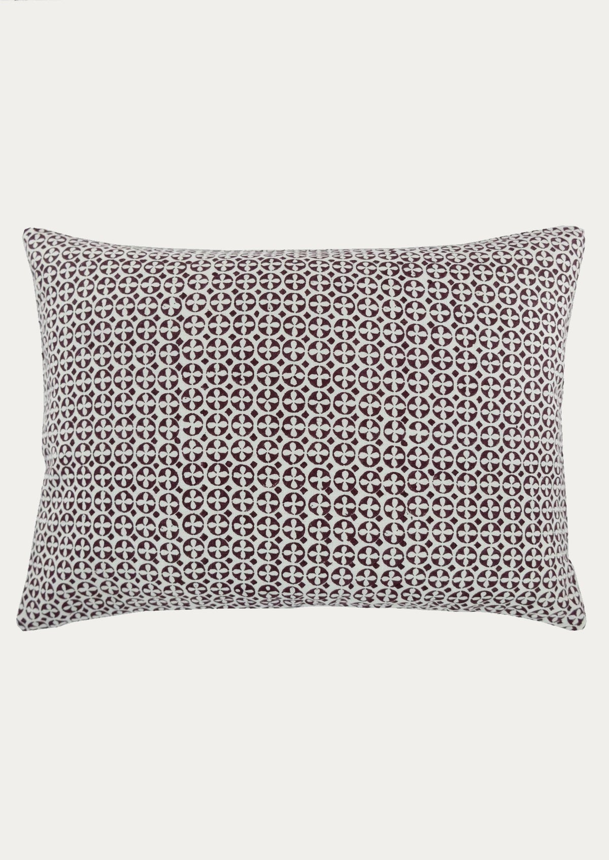 A lumbar throw pillow in white with geometric circular block print pattern in brown.