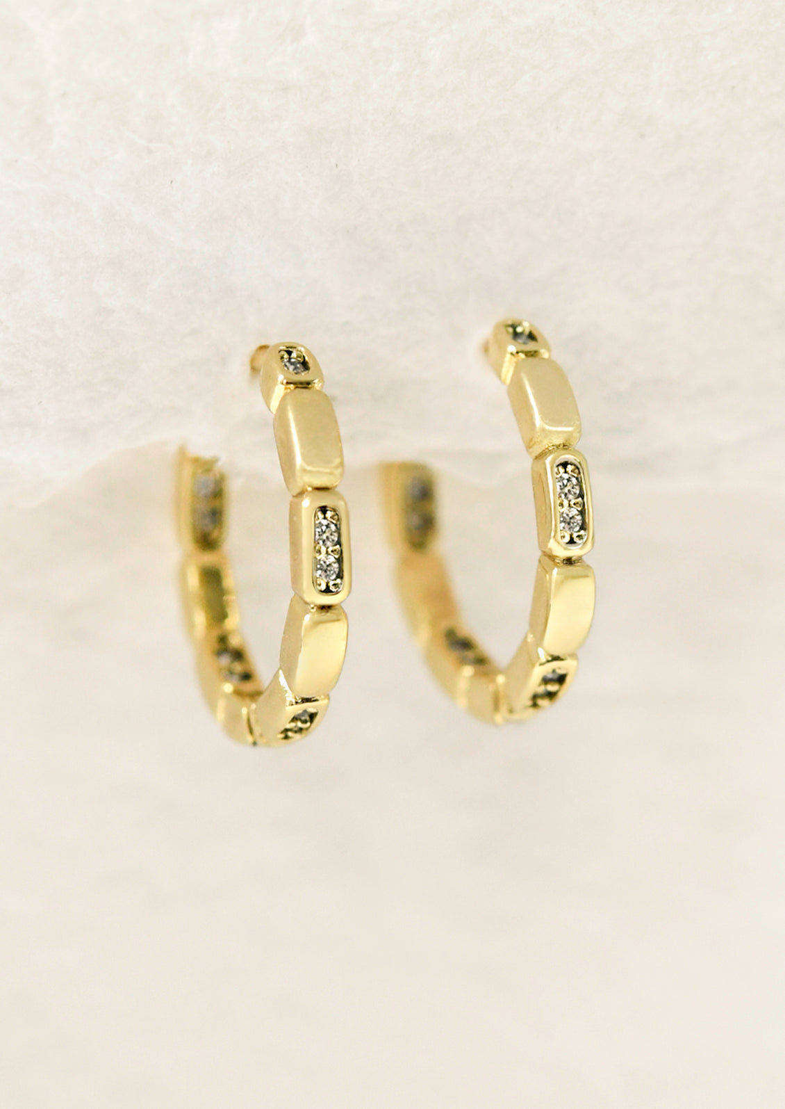 A pair of gold huggie hoop earrings with glass crystals.