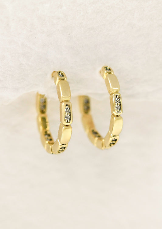 A pair of gold huggie hoop earrings with glass crystals.