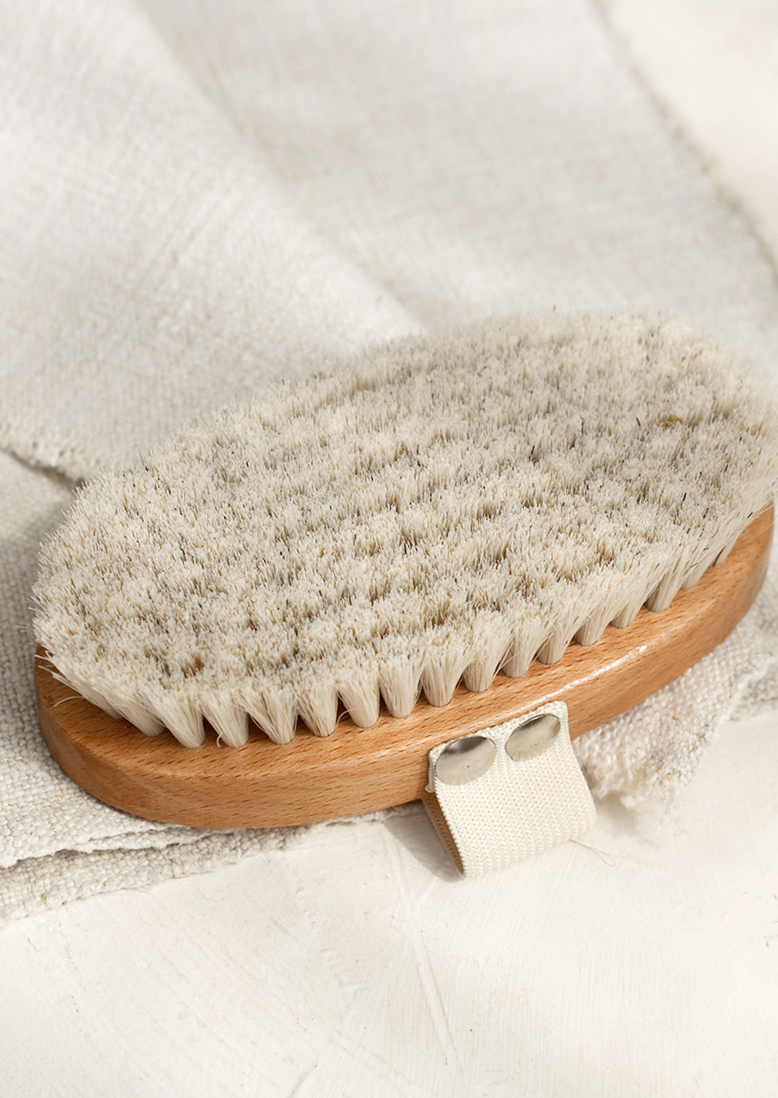 An oval shaped wood and bristle bath brush with elastic hand strap.