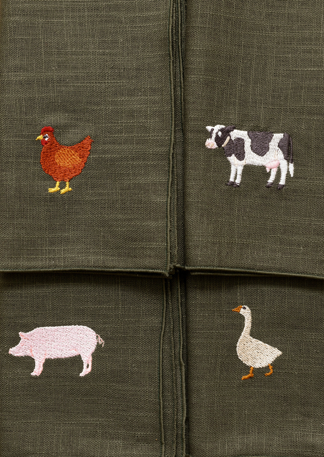 Set of four green napkins with embroidered animal designs on a matching green background.