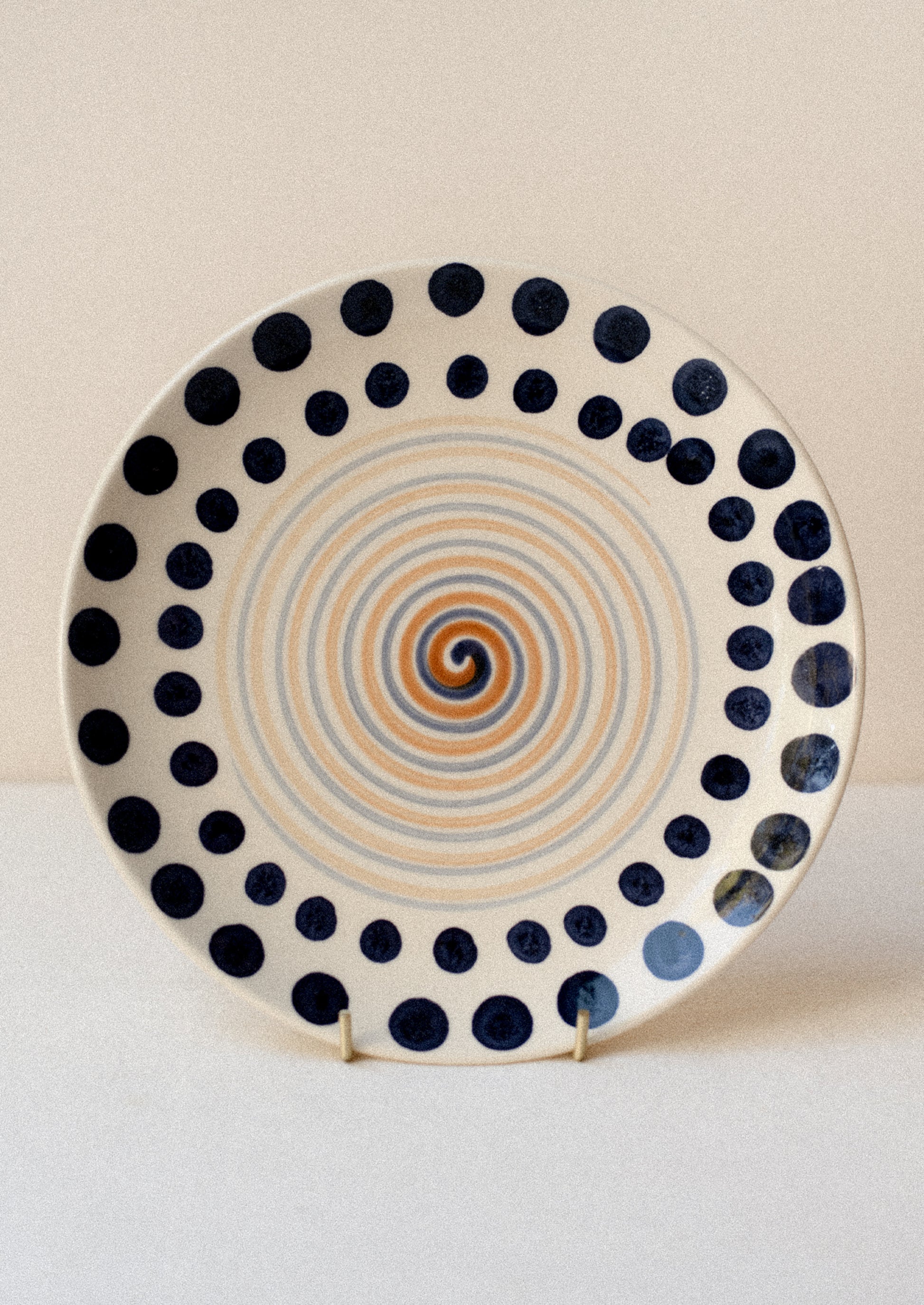 A plate with hand painted geometric swirl and dot pattern in navy blue and brown.