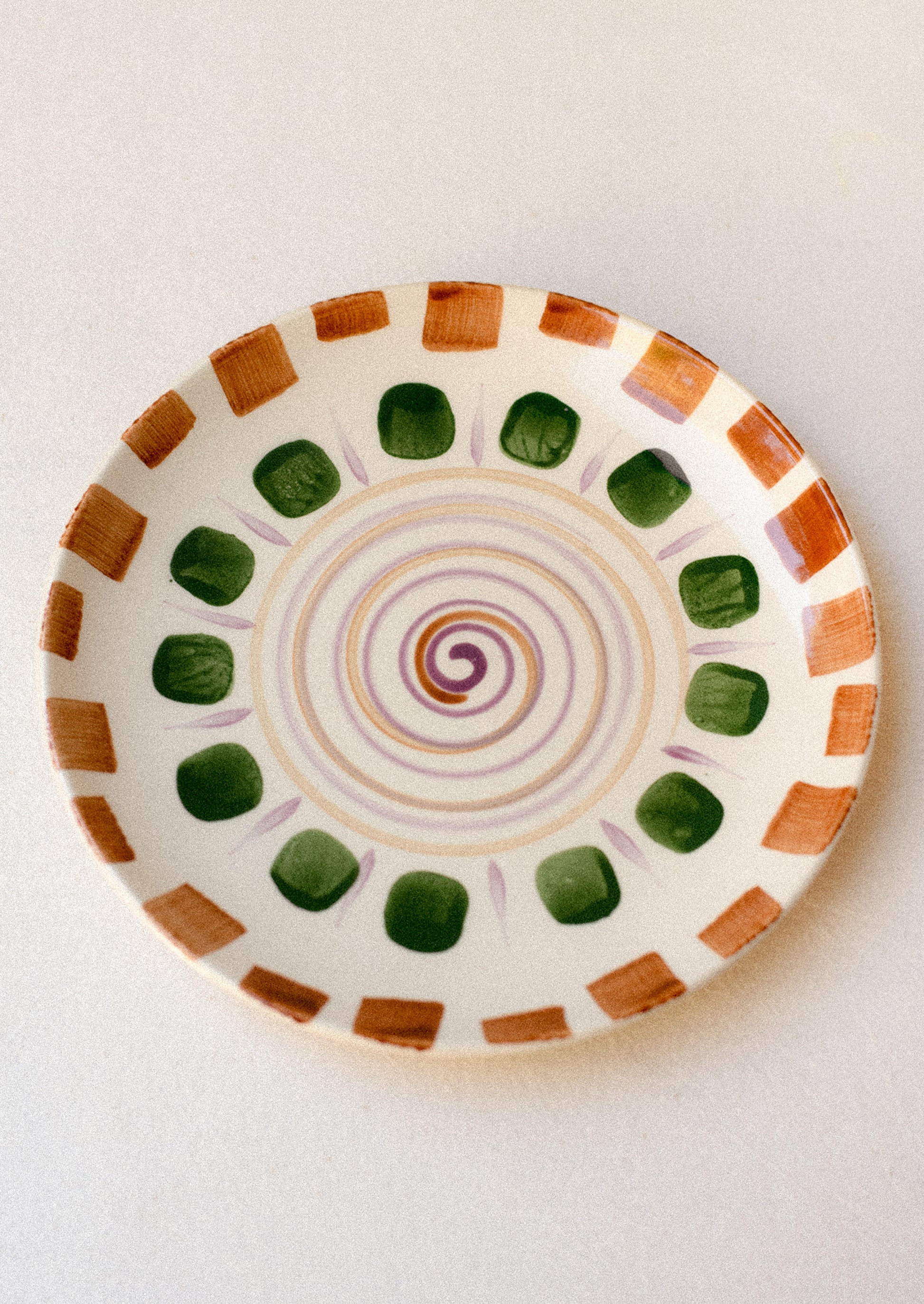 A plate with hand painted geometric swirl and square pattern in brown, green and purple.