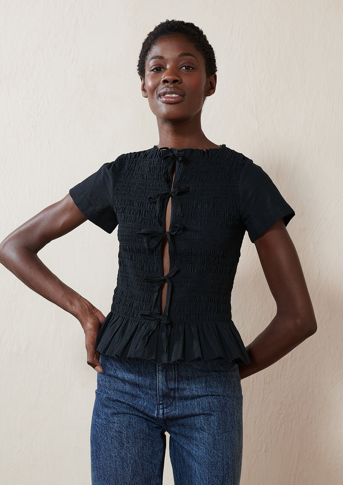 A woman wearing a smocked black short sleeve top with ties in front.