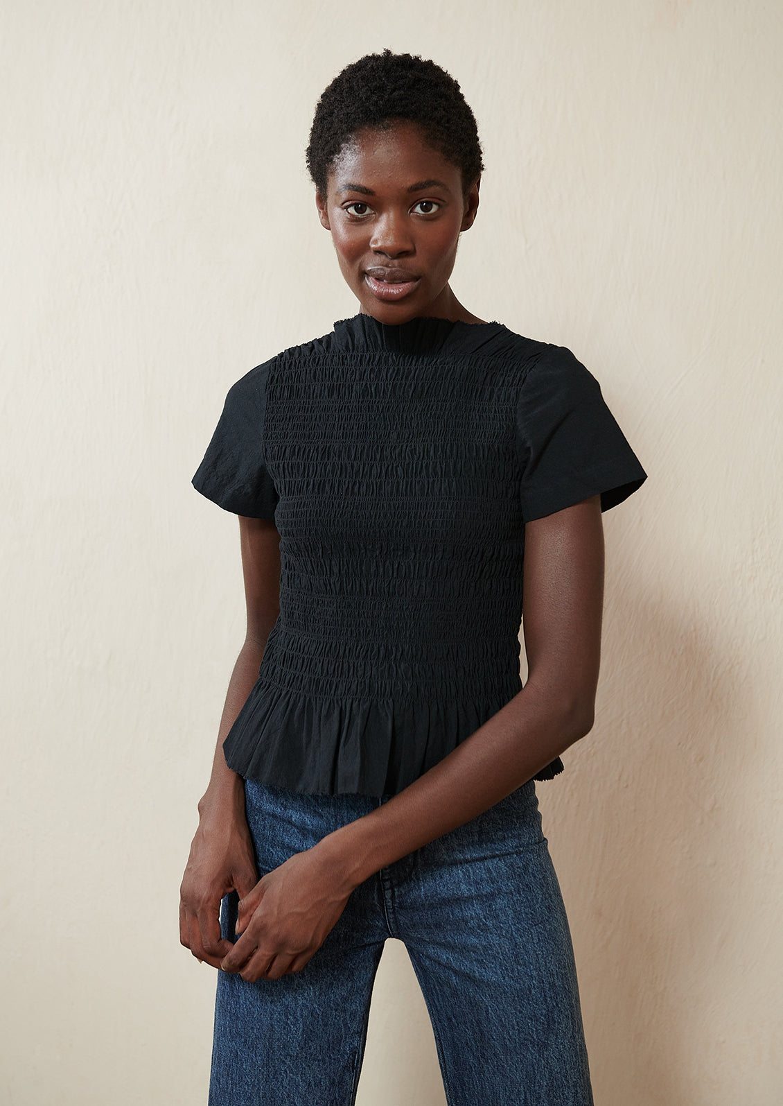A woman wearing a smocked black short sleeve top.