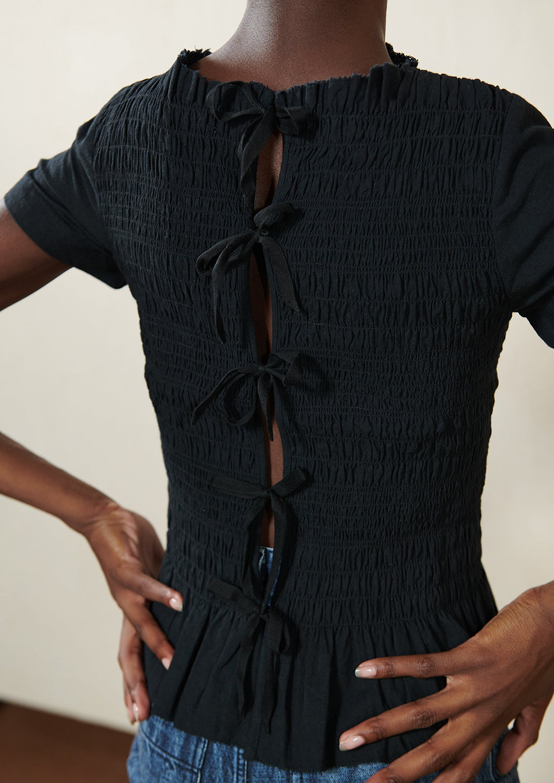 A woman wearing a smocked black short sleeve top with ties in back.