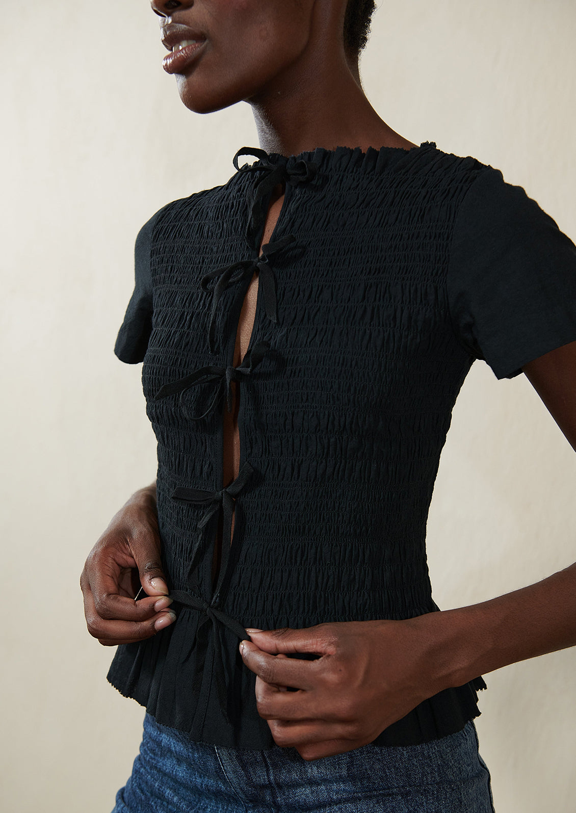 A woman wearing a smocked black short sleeve top with ties in front.