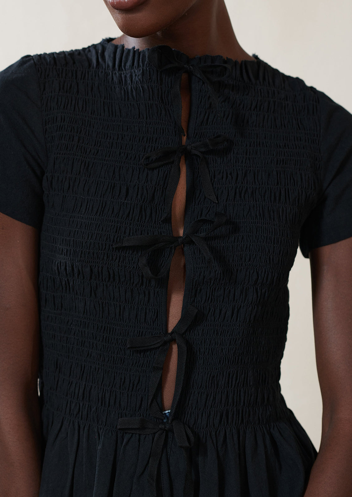 A woman wearing a smocked black short sleeve top with ties in front.