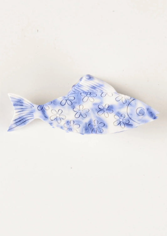 A blue and white hair claw in the shape of fish with carved floral pattern.