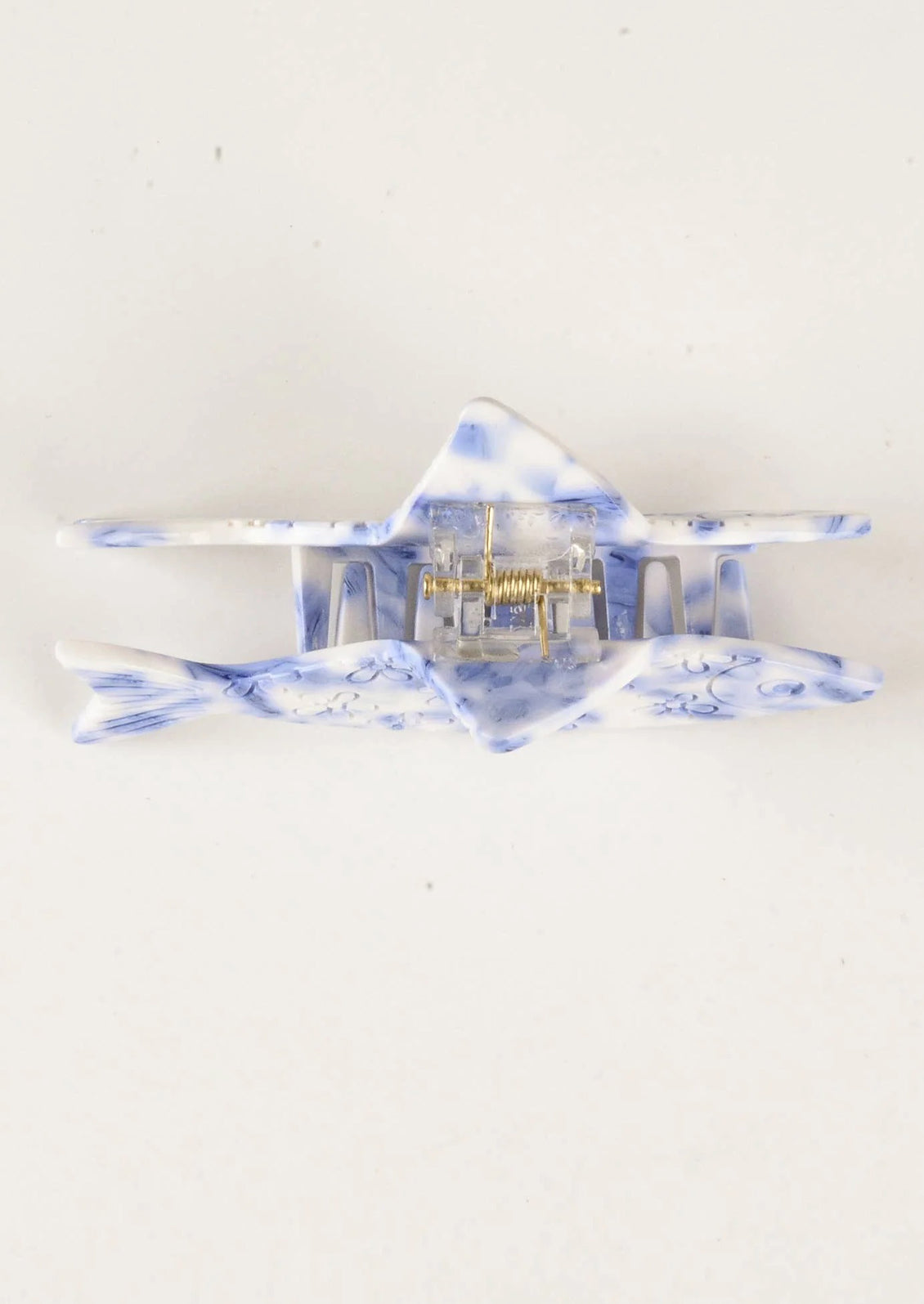 A blue and white hair claw in the shape of fish with carved floral pattern.
