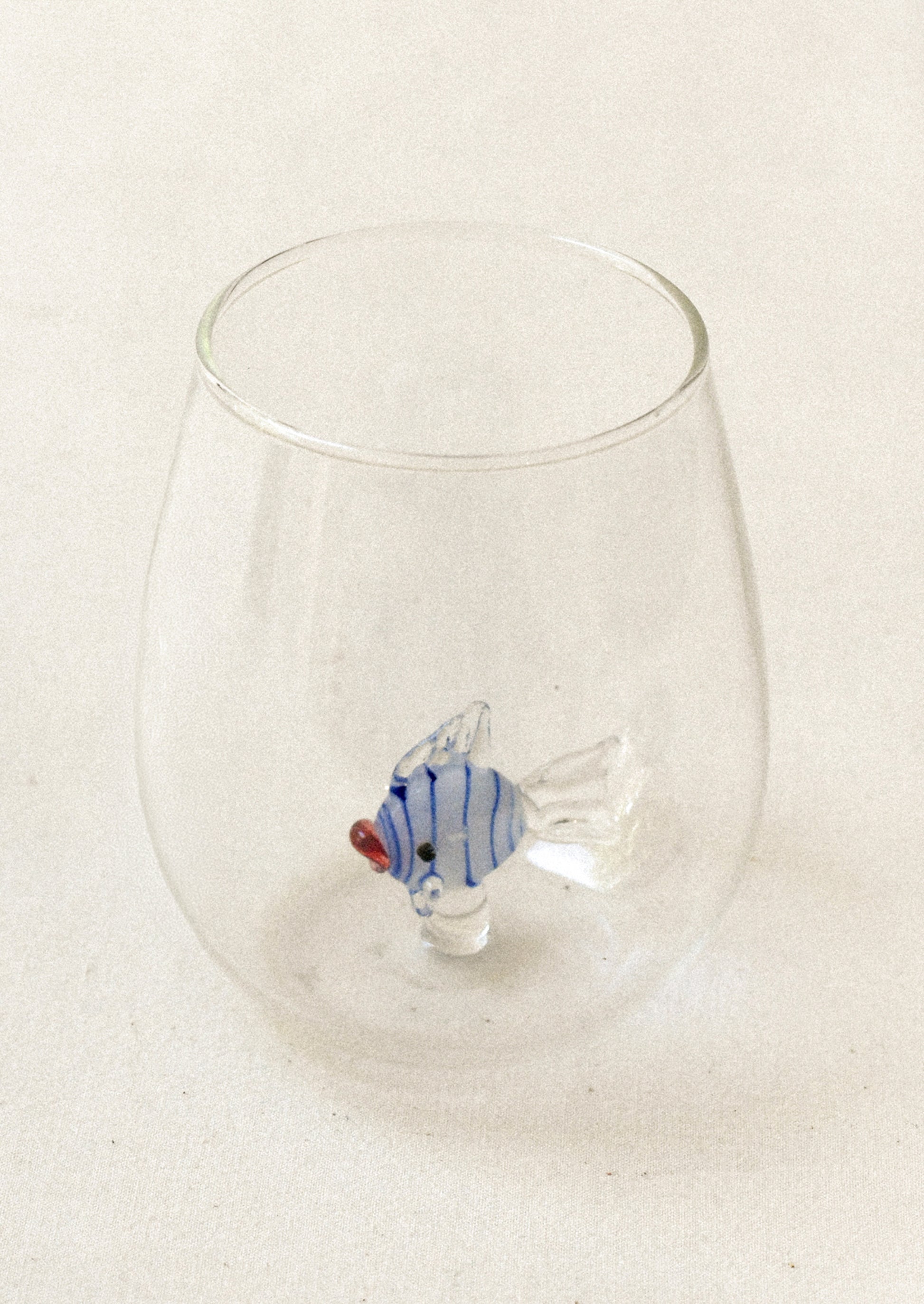 A clear tumbler glass with lampwork fish detail at inner bottom.