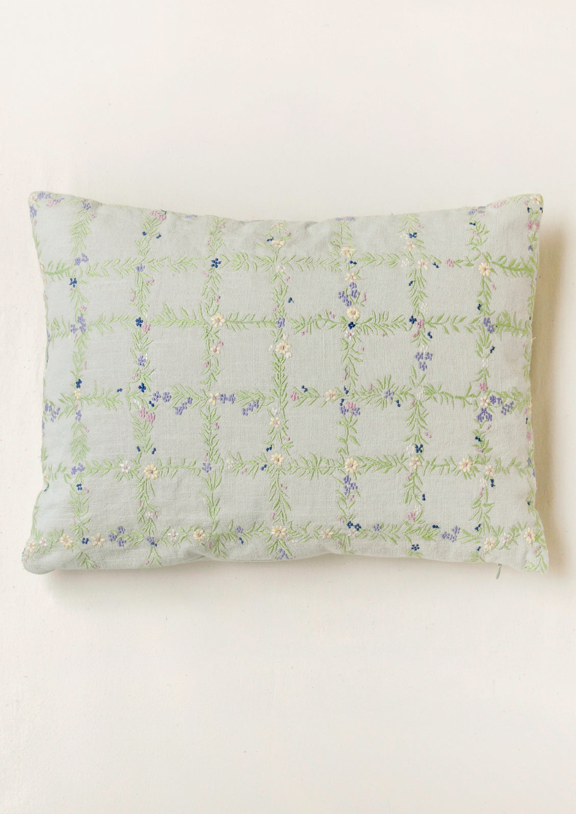 A light blue pillow with an embroidered floral grid pattern.