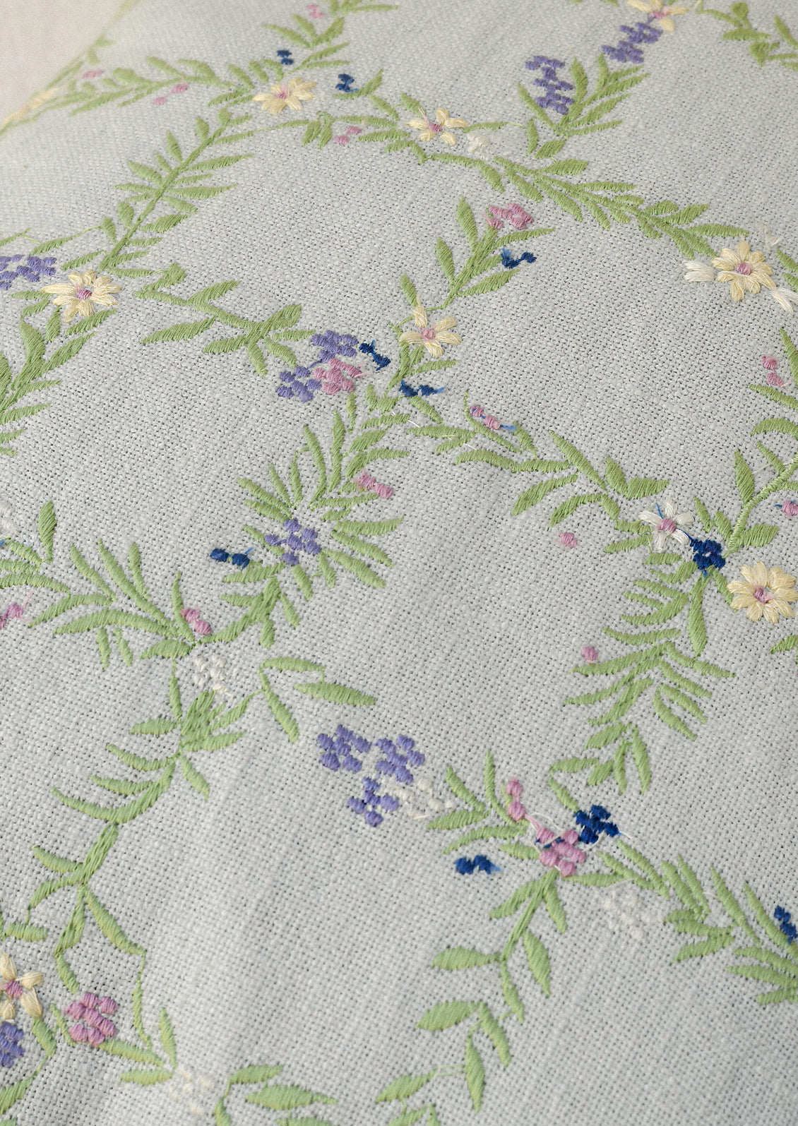 Closeup of a light blue pillow with an embroidered floral grid pattern.