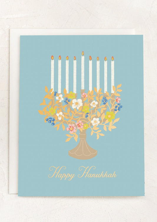 A blue card with image of floral menorah, text reads "happy hanukkah".